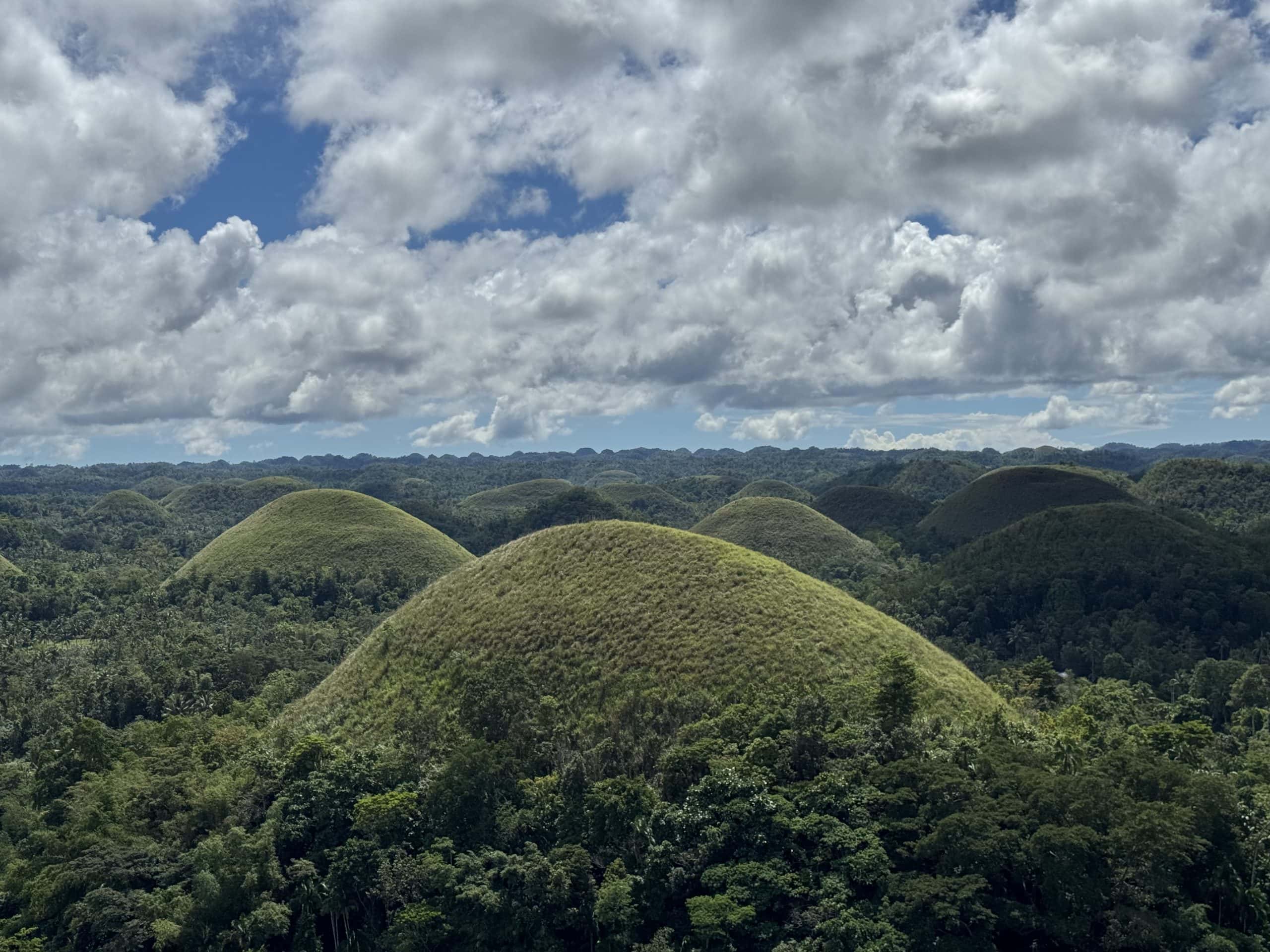 Aerial view of the Chocolate Hills in Bohol, showcasing over 1,200 cone-shaped hills covered in green grass.