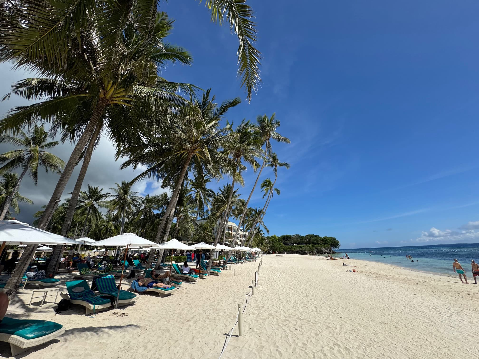 White sand and turquoise waters of Alona Beach in Bohol, with beachfront resorts and diving shops.