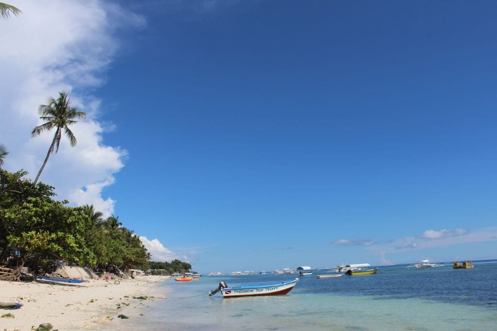 A beach in Bohol with boats and bright blue sky and light blue water.
