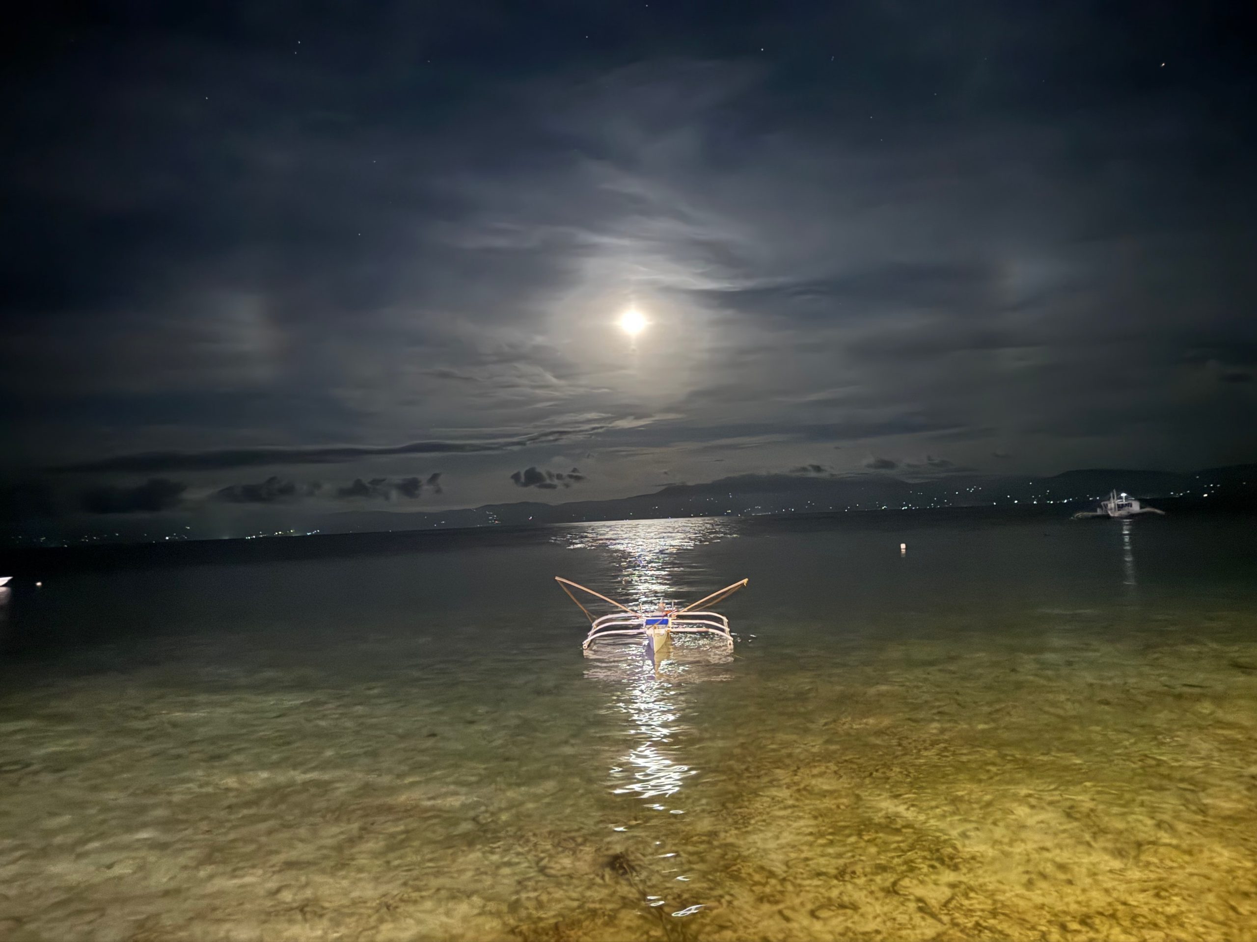 Calm ocean view from the rocky edge of Panagsama Beach in Moalboal at night.