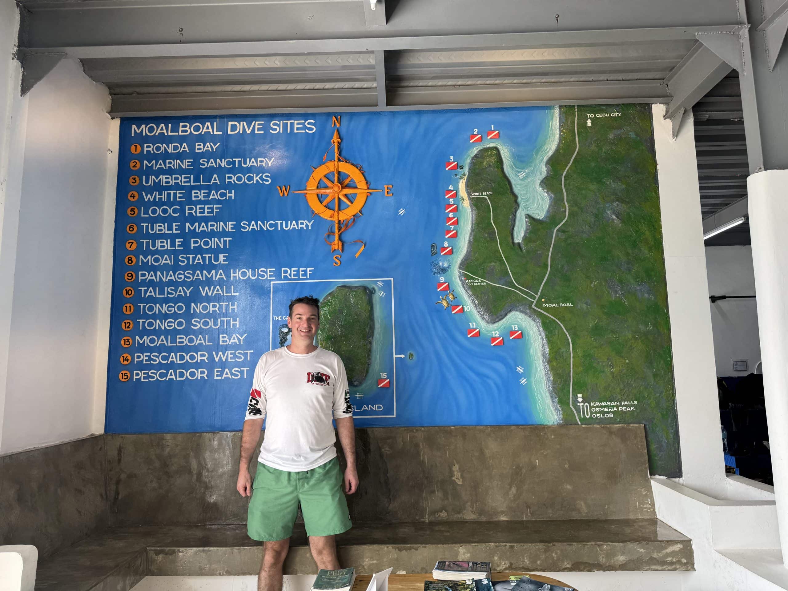 Ryan Gillard from the Global Travel Blog outside of a dive map of the Moalboal, Cebu dive sites.