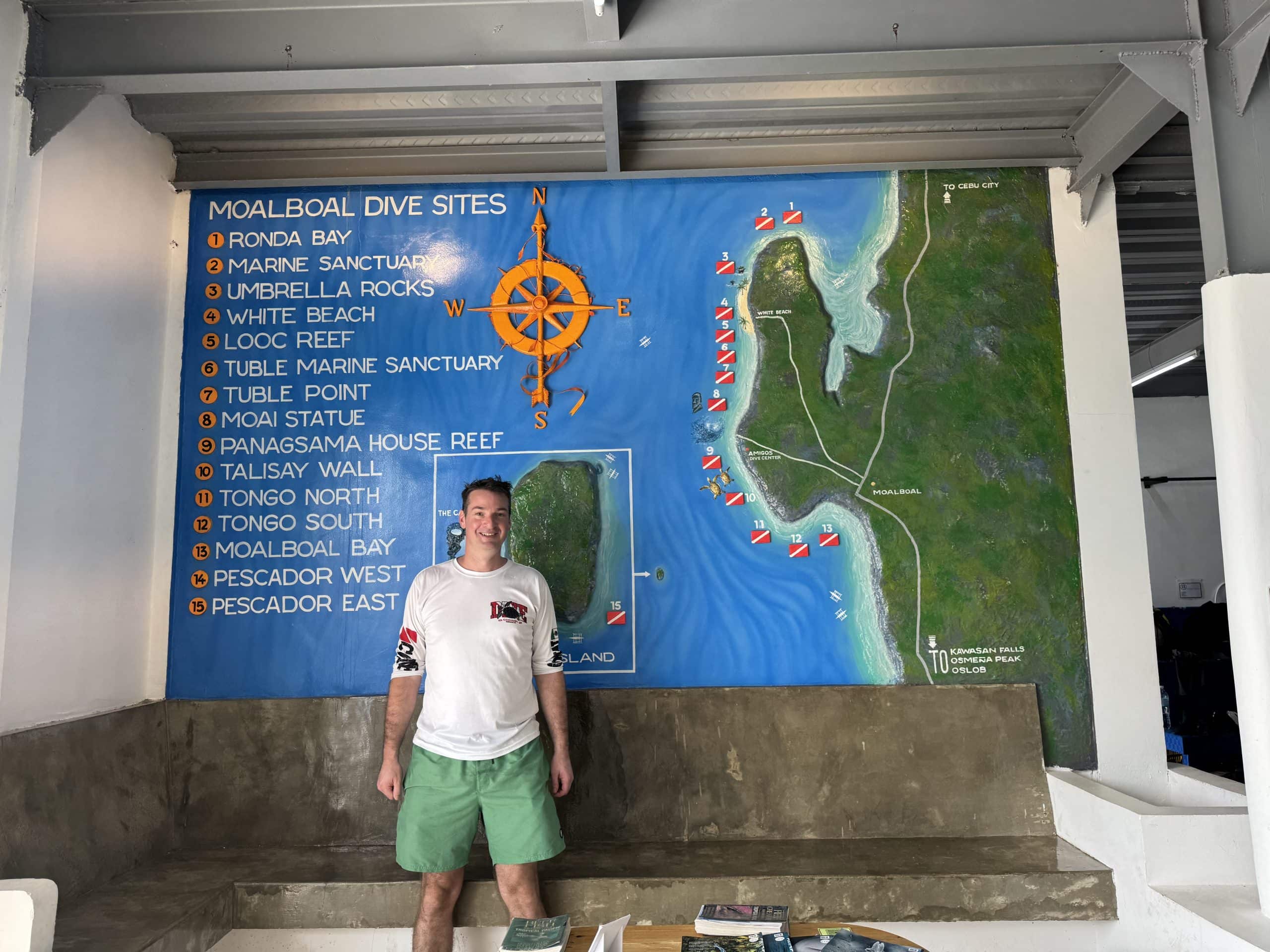 Ryan Gillard posing outside a dive site map of Moalboal, Cebu, Philippines.