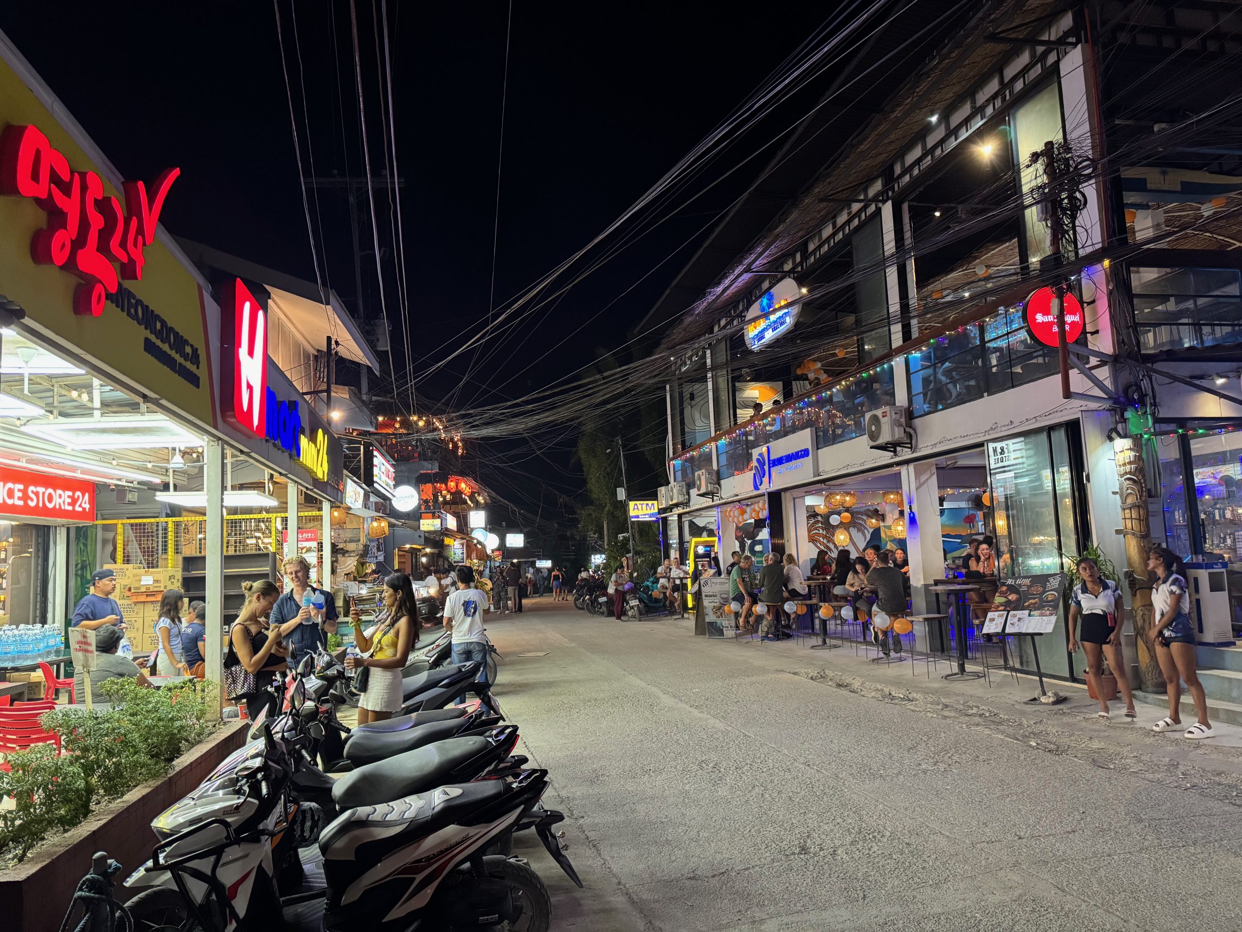 The main tourist street of Moalboal at night with onlookers and pedestrians.