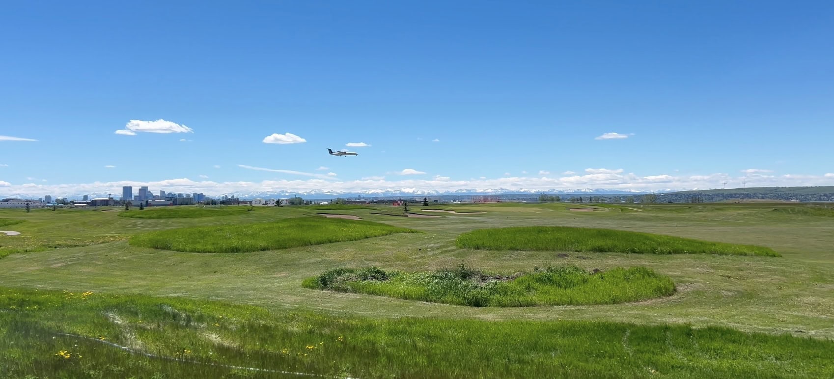 A plane landing at Calgary International Airport with downtown Calgary and the Rocky Mountain in the distance on a warm and sunny day.