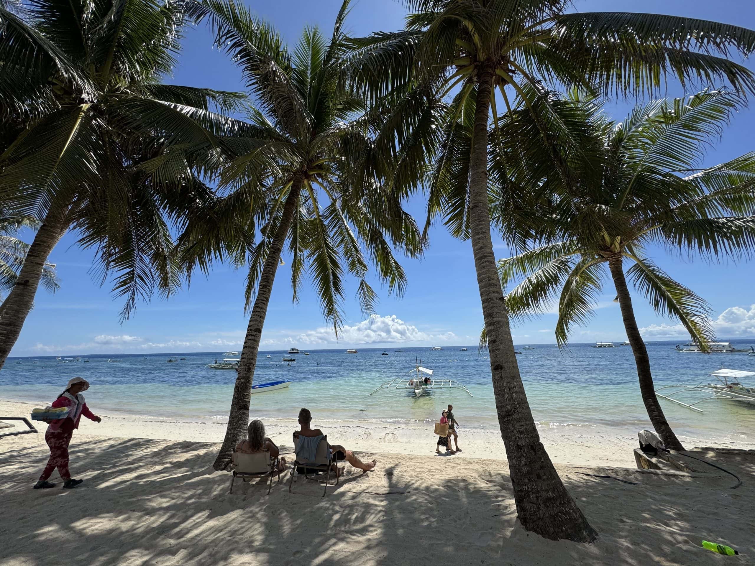 Tranquil white sand beach with clear water and traditional banca boat in the Philippines.