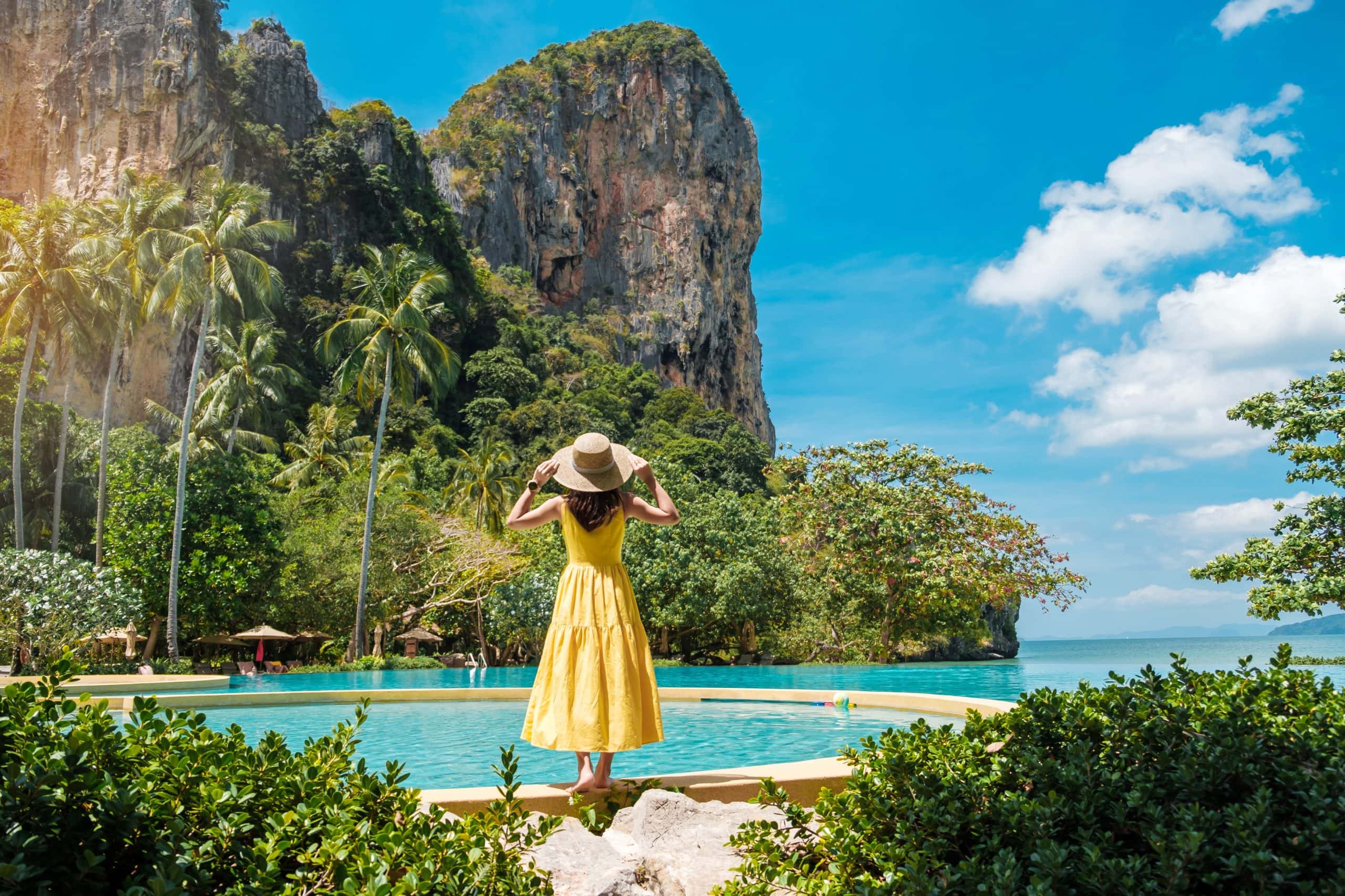Young female traveler in a yellow dress and hat enjoying tropical island views