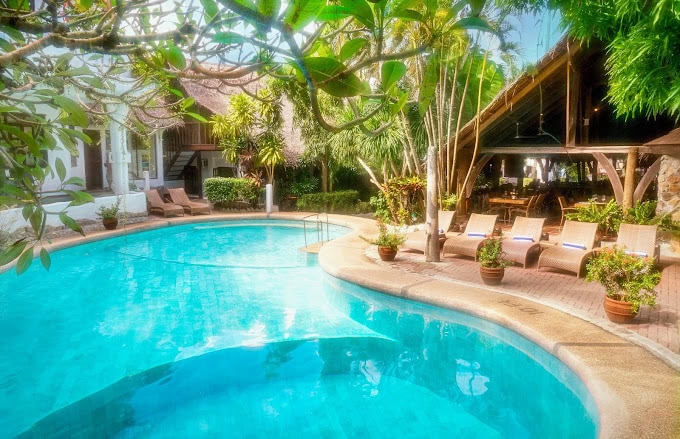 Tropical poolside area at Atlantis Puerto Galera Resort in Sabang, surrounded by lush greenery, sun loungers, and thatched-roof buildings designed for diver relaxation.