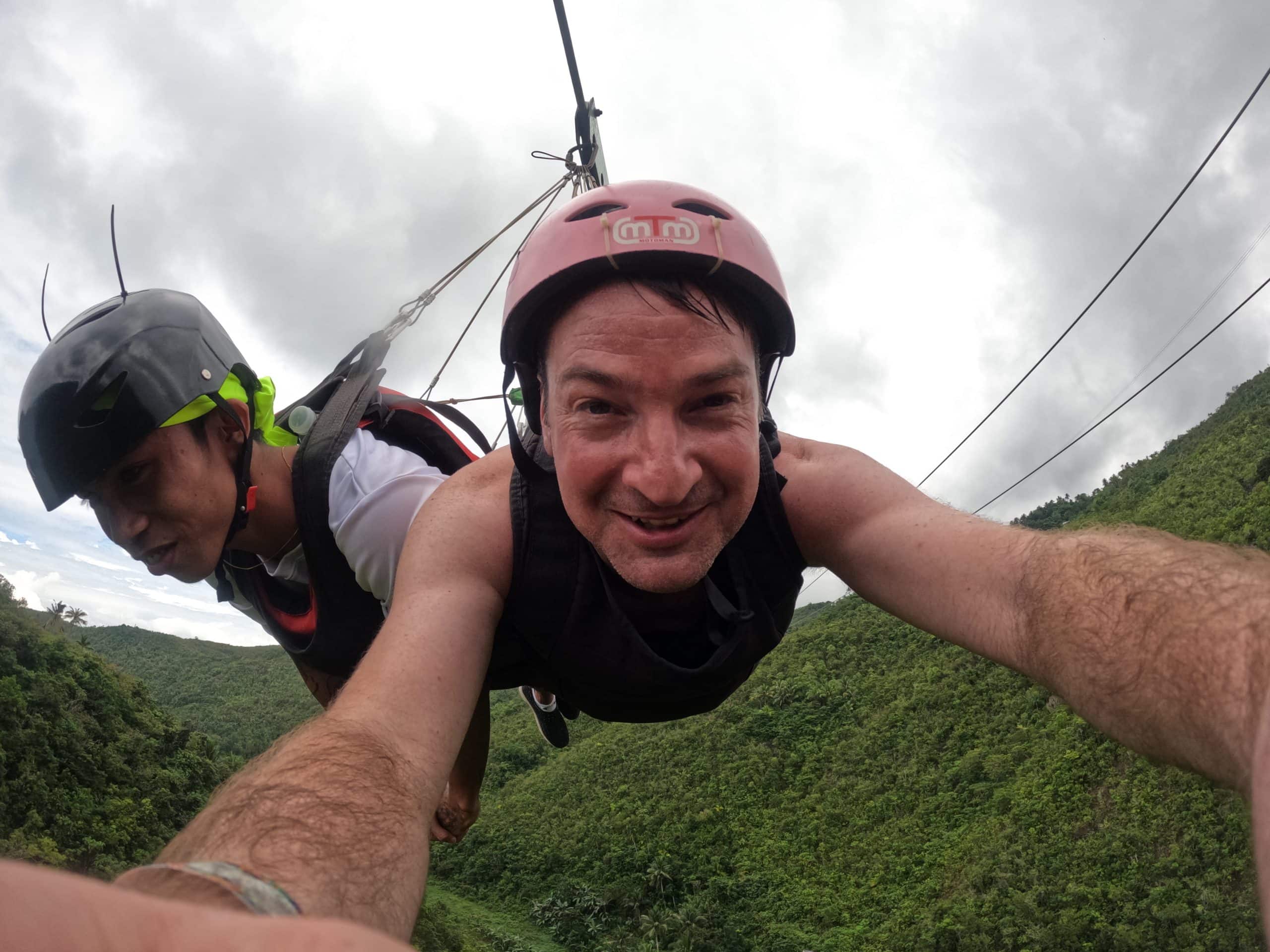 Tourist ziplining over lush jungle near Kawasan Falls, a popular adrenaline-filled add-on to the canyoneering adventure from Moalboal, Philippines.