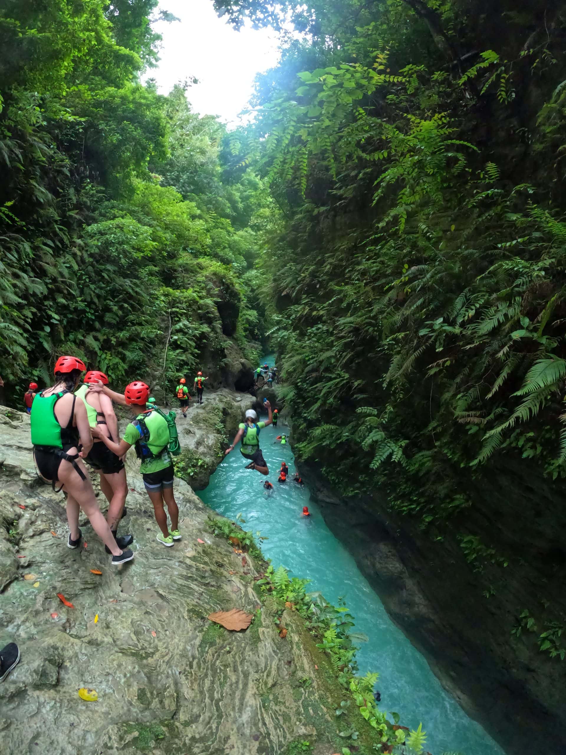 Group of canyoneers navigating a narrow jungle canyon with turquoise water near Kawasan Falls, one of the best outdoor adventures in Moalboal, Philippines.