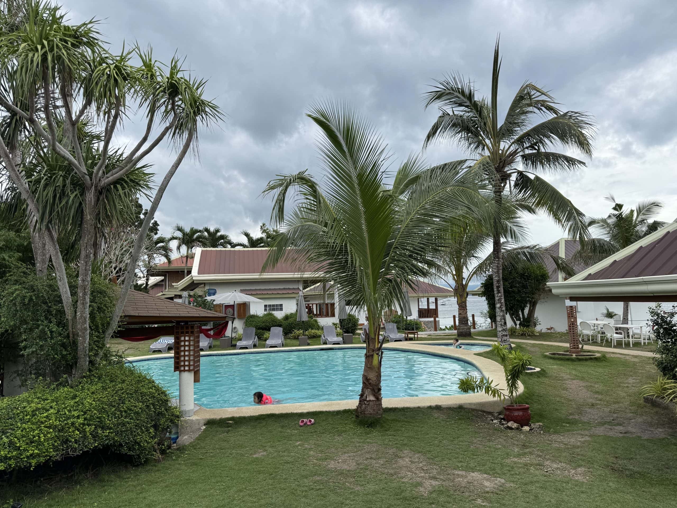 Poolside view of a tropical resort in Moalboal, Cebu, surrounded by palm trees — a relaxing place to stay before or after your Kawasan Falls canyoneering adventure.
