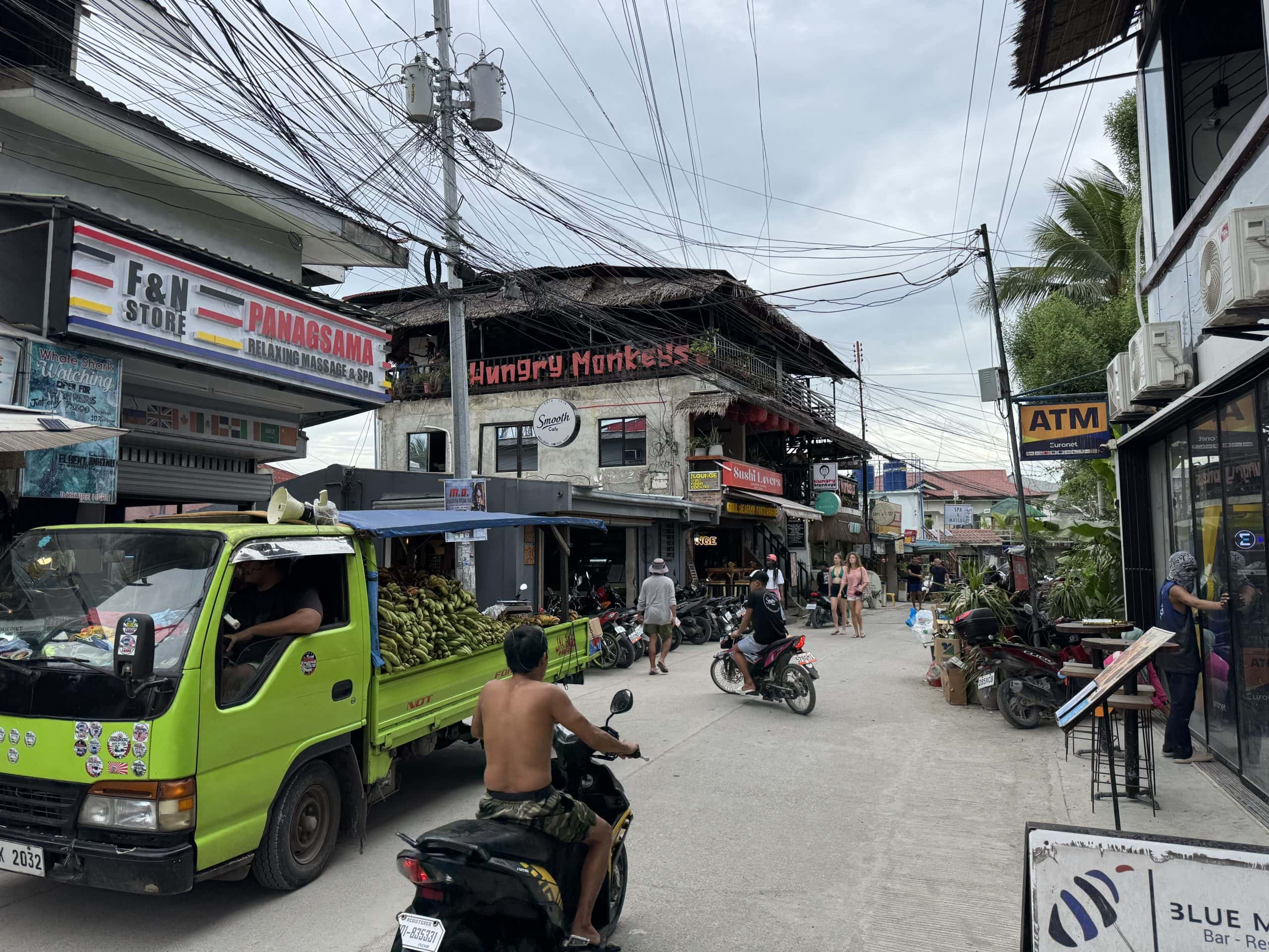 bustling street in panagsama beach moalboal with scooters banana truck hungry monkeys bar and atm signs