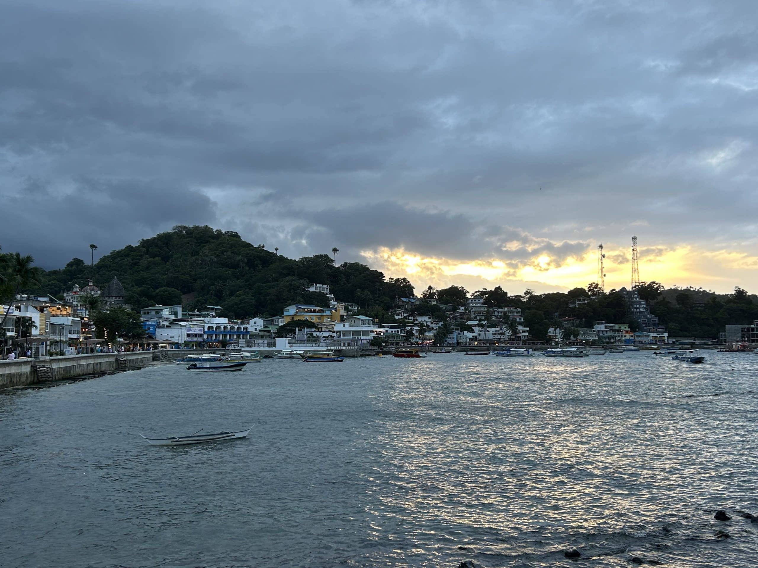 sunset view over Sabang Bay in Puerto Galera with boats anchored near the waterfront and hillside buildings lit by golden light