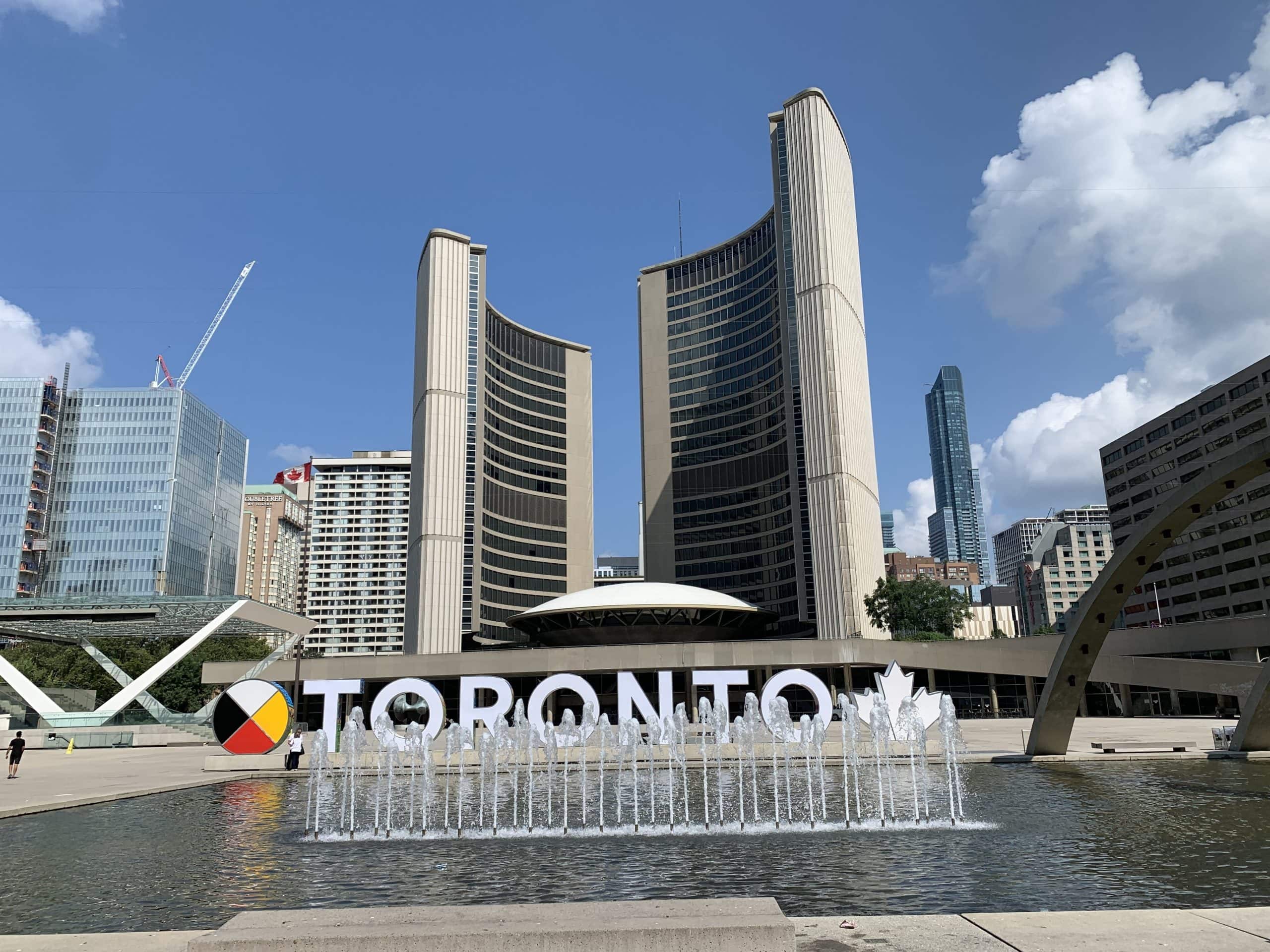 Toronto sign and city skyline in the background with visitors taking photos