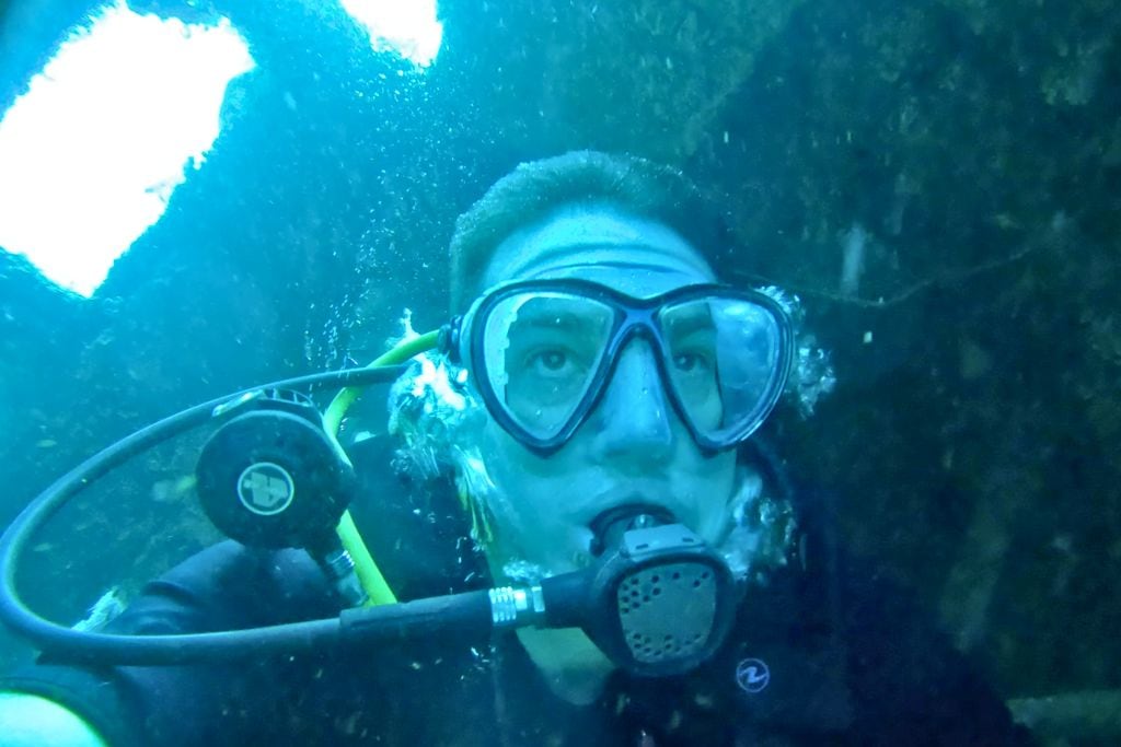 scuba diver exploring an underwater cavern in Sabang, Puerto Galera with mask and regulator in view and light filtering from above