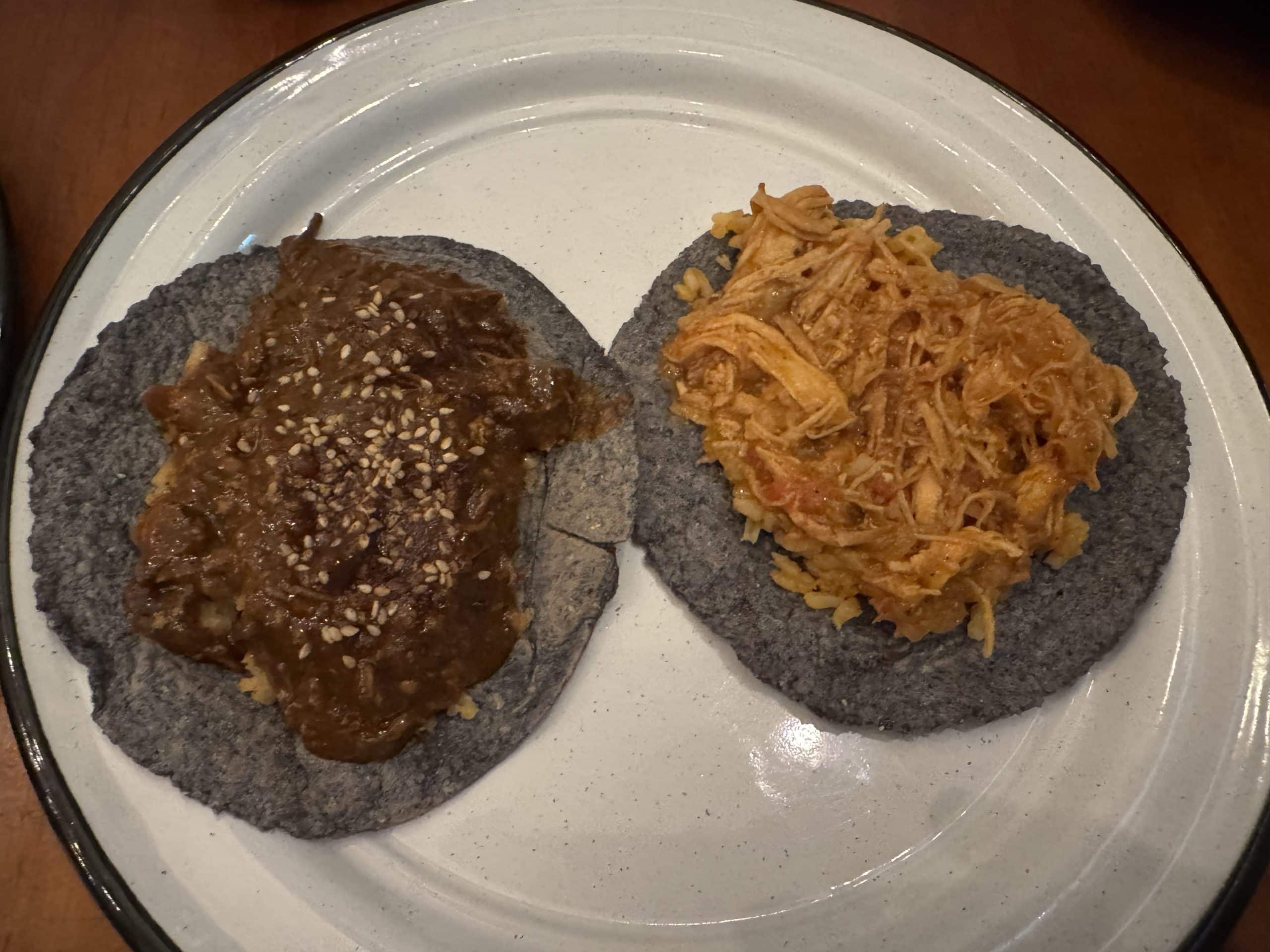 Close-up of two tacos on blue corn tortillas topped with mole and shredded chicken, served at a local eatery in Cozumel, Mexico.