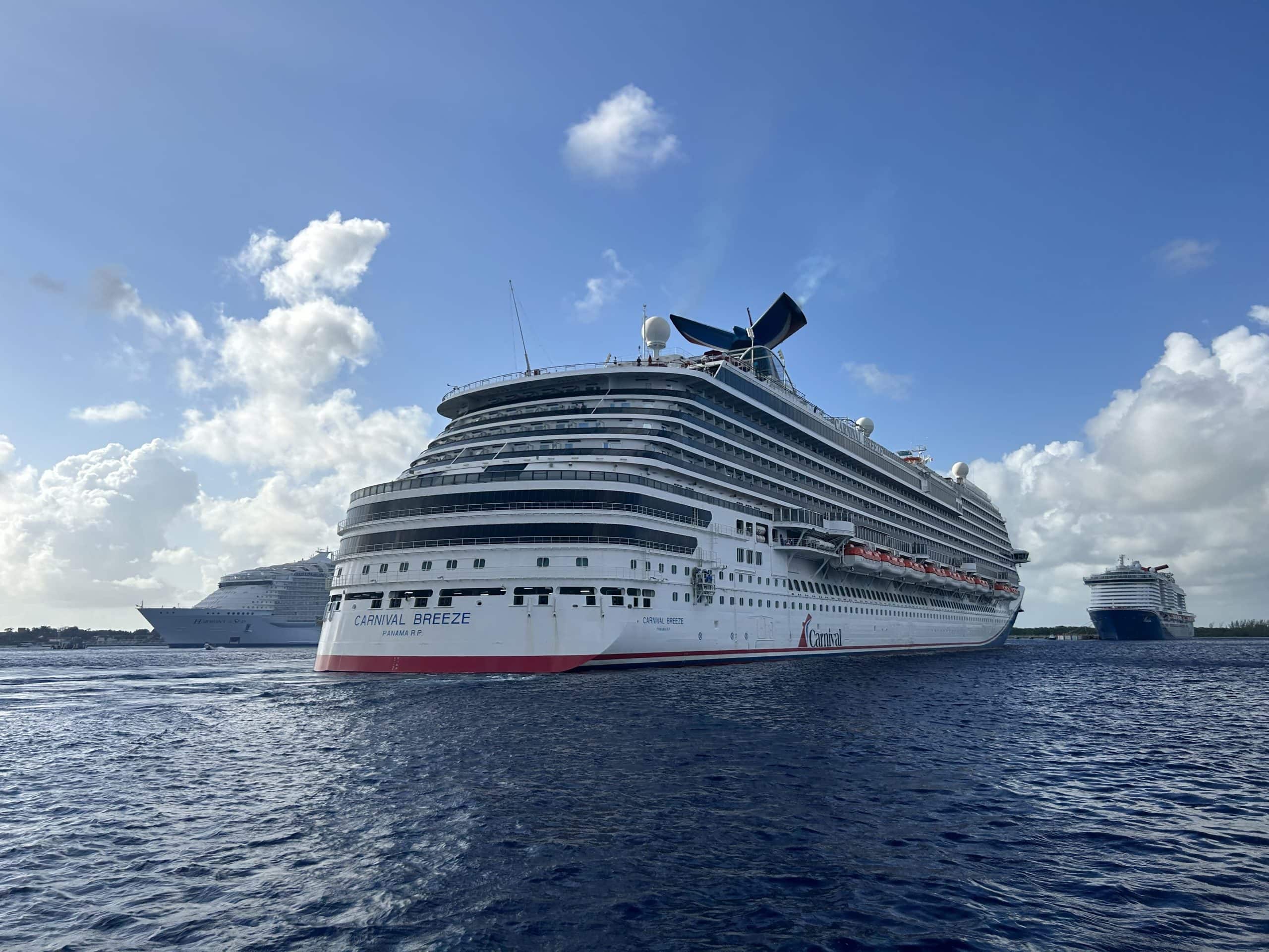 Carnival Breeze cruise ship docked off the coast of Cozumel, Mexico, with two other large cruise ships in the background under a bright blue sky.