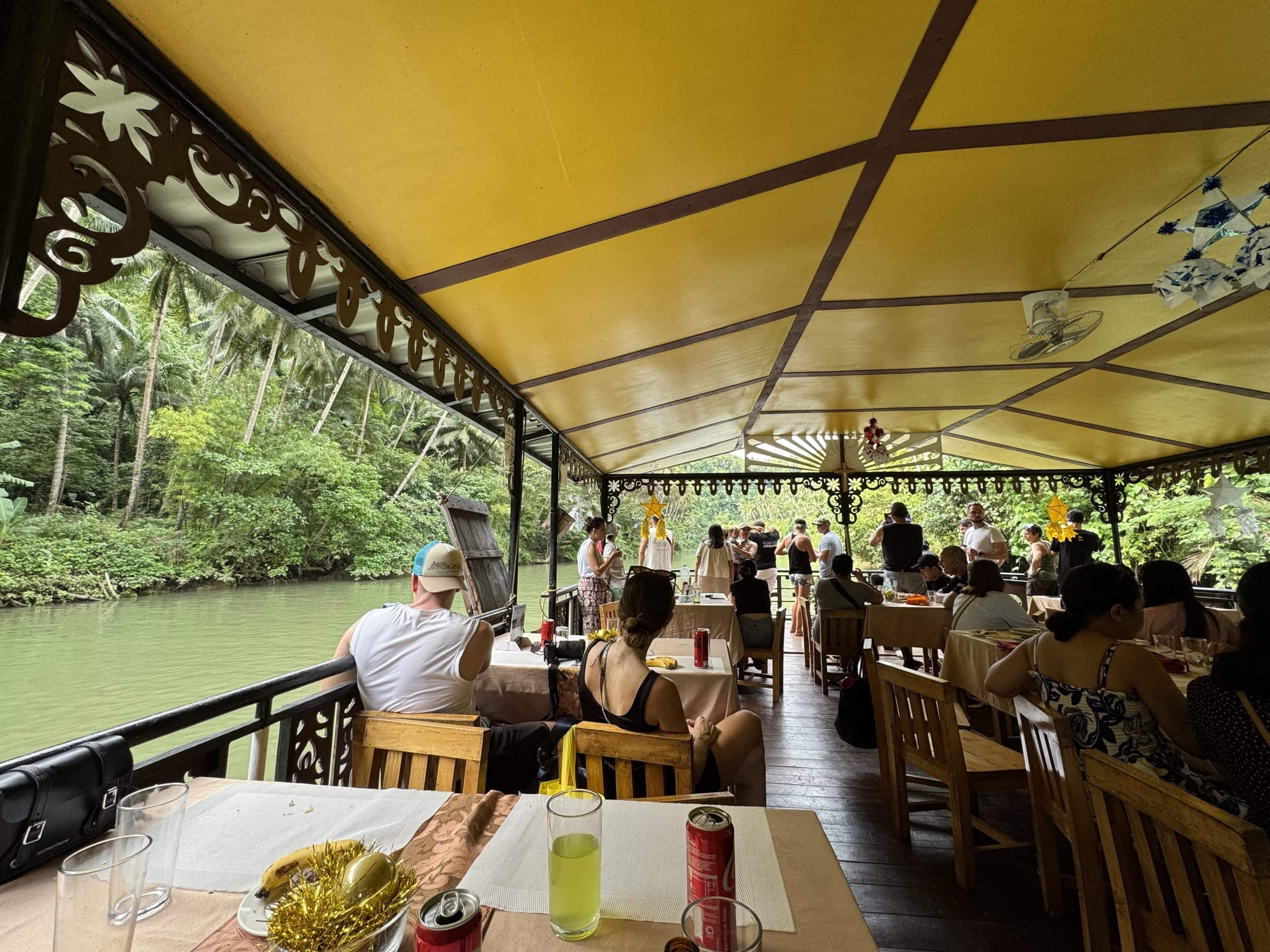 Tourists enjoying a floating restaurant experience on the Loboc River in Bohol, Philippines with live music, local food, and lush jungle views along the riverbank