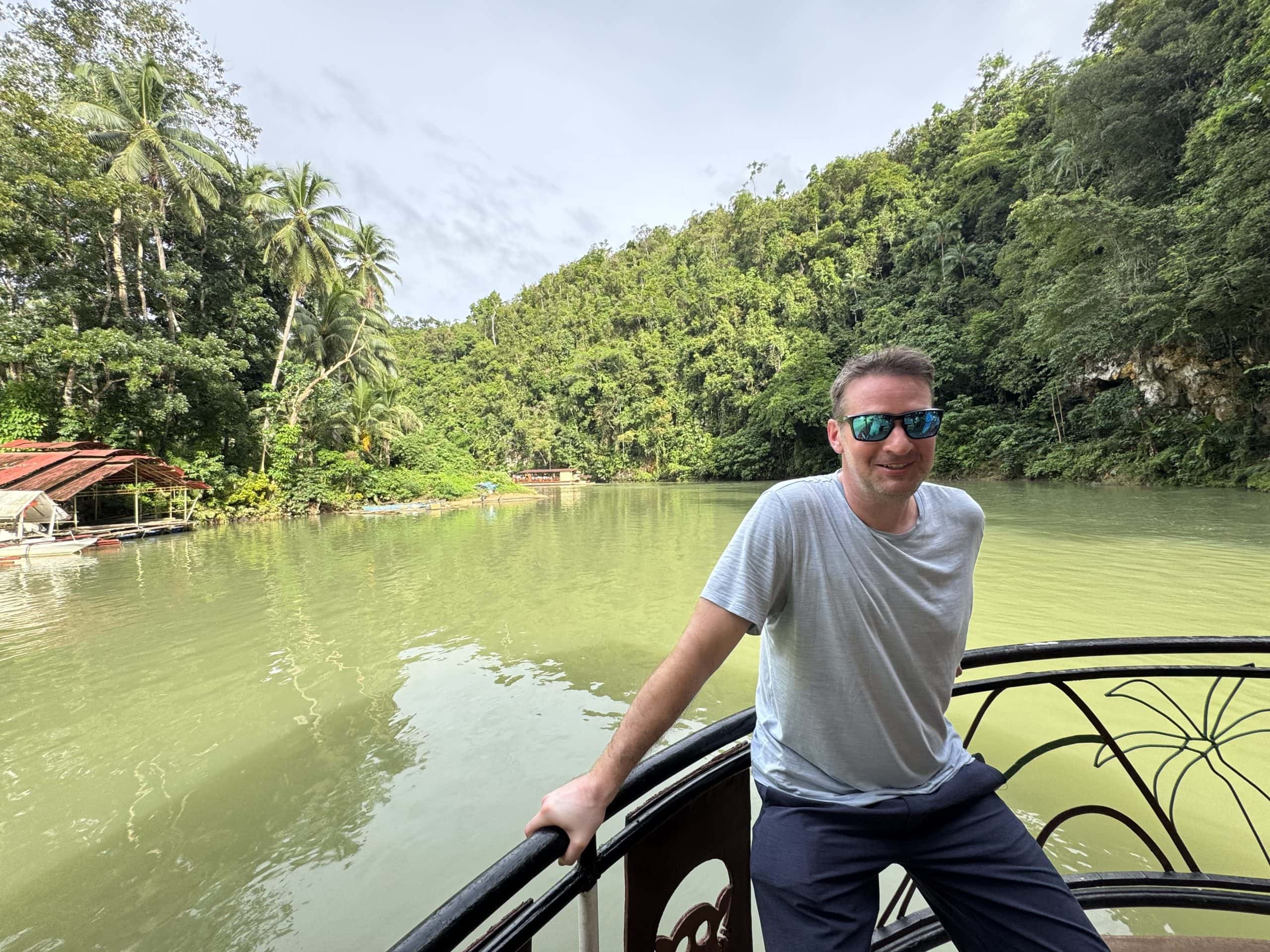 Man relaxing on a boat ride along the Loboc River in Bohol, Philippines surrounded by lush tropical jungle and calm green water