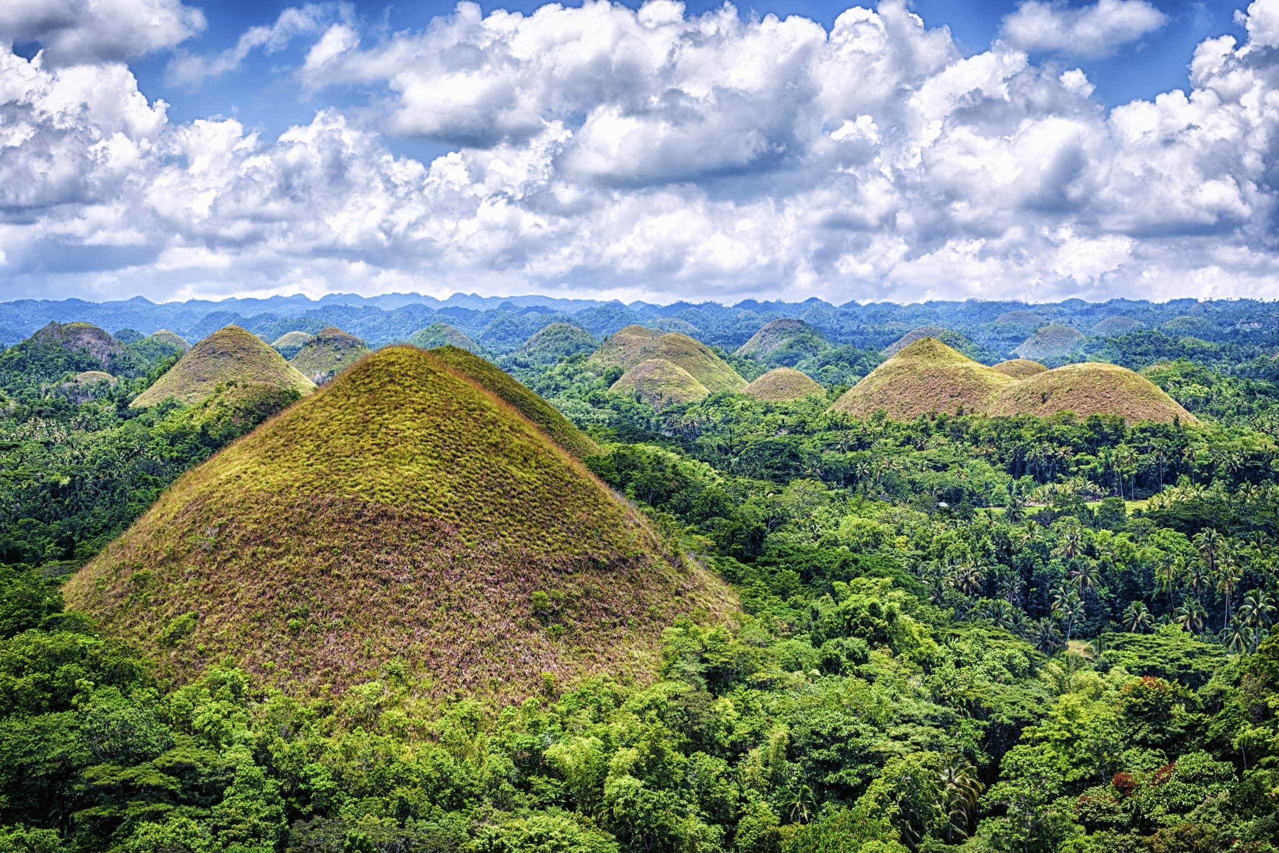 Scenic view of the Chocolate Hills in Bohol, Philippines with lush green vegetation, rolling hills, and a dramatic sky filled with clouds