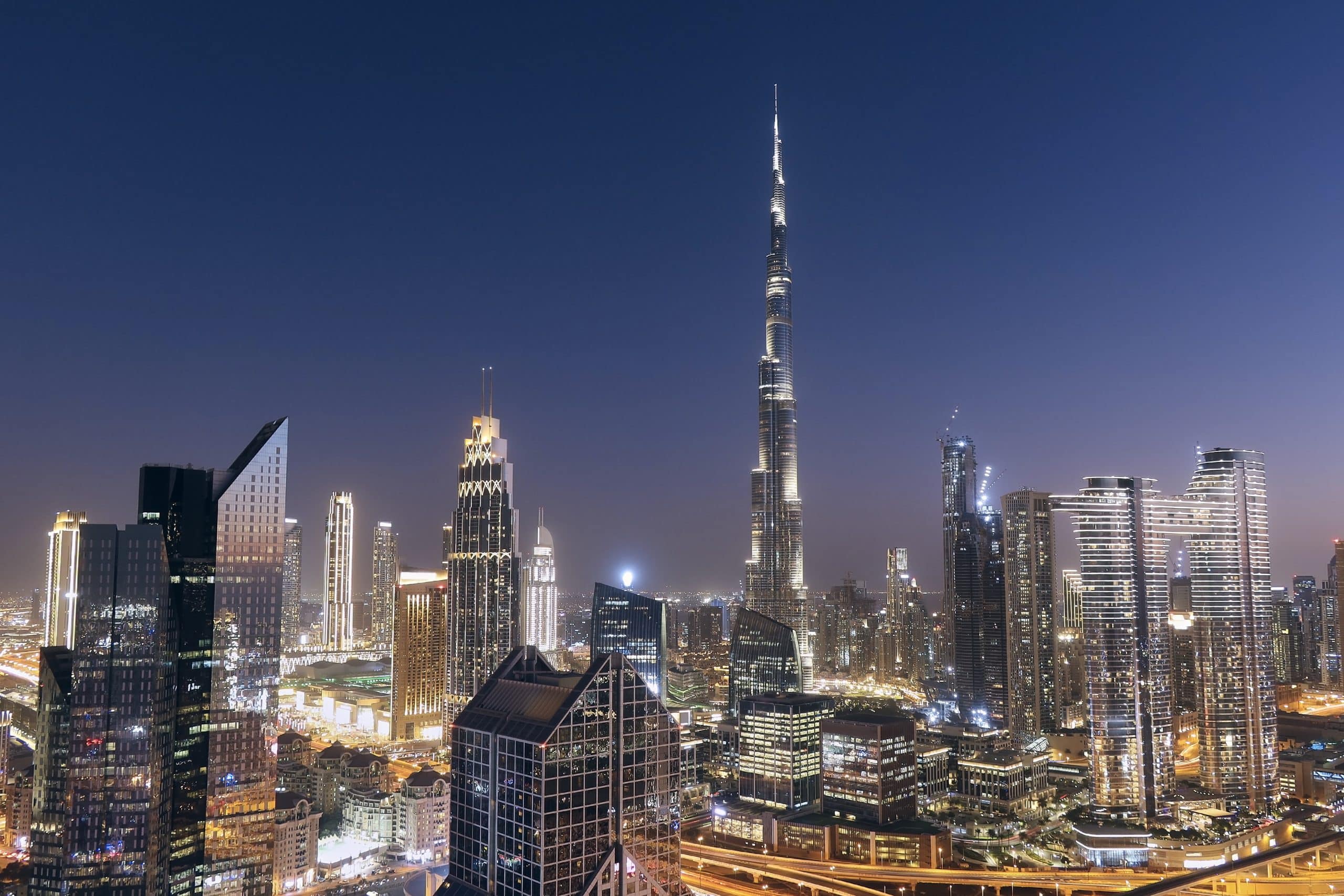 Stunning night view of Dubai’s modern skyline with the illuminated Burj Khalifa towering above the city, surrounded by glittering skyscrapers and vibrant city lights.