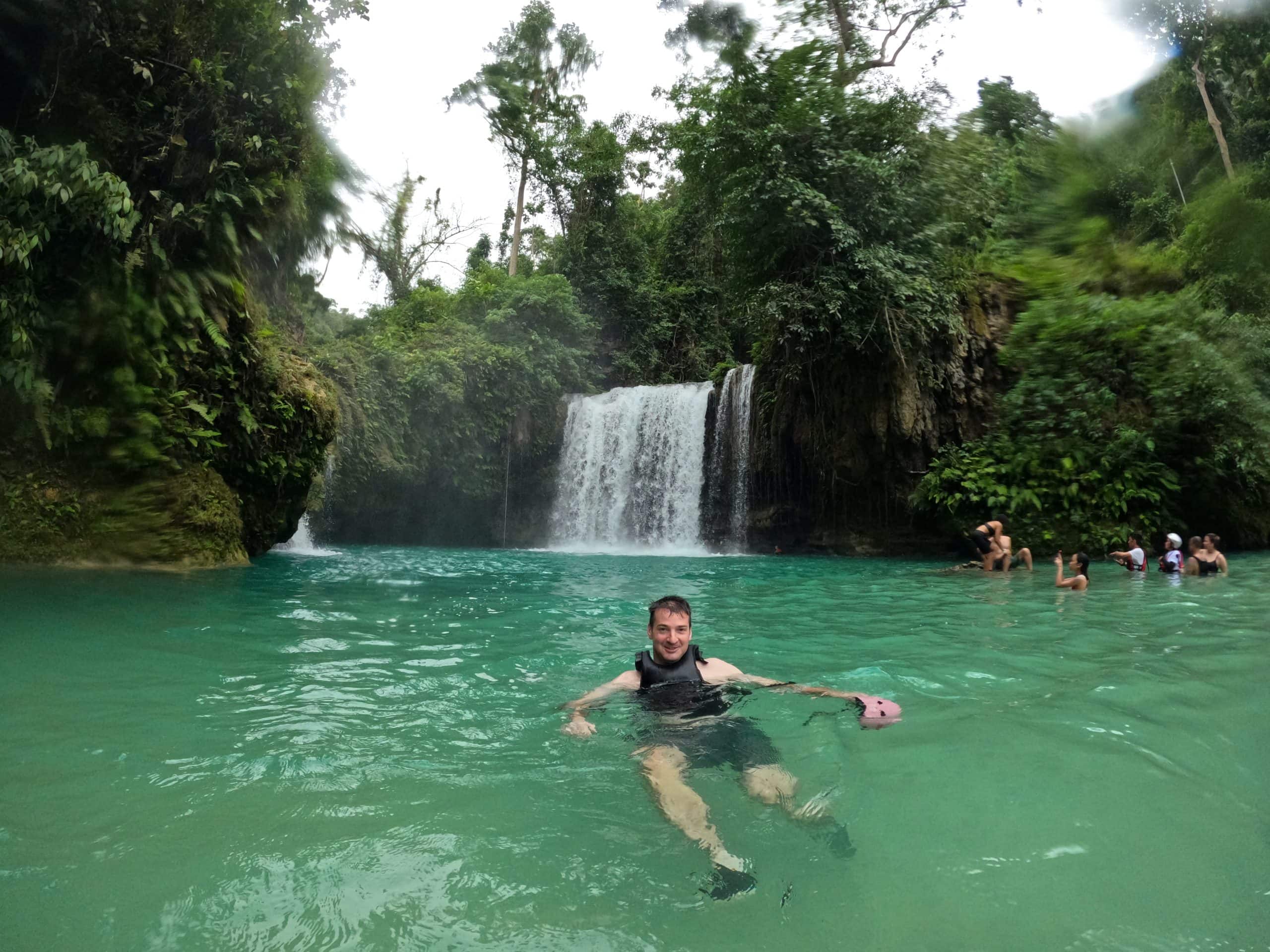 A traveller relaxes in the turquoise pool at Kawasan Falls in Badian, Cebu, surrounded by lush jungle and cascading waterfalls.