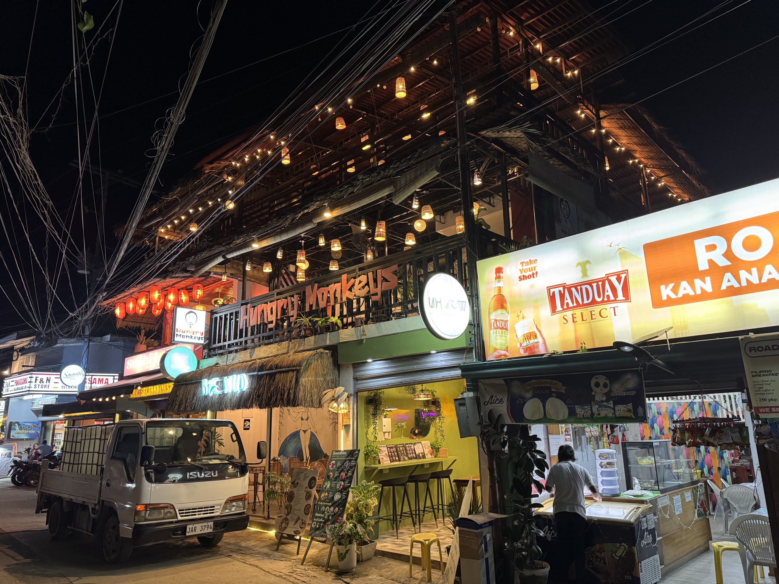 The lively Panagsama nightlife scene in Moalboal, Cebu, featuring the popular Hungry Monkey bar and nearby restaurants glowing with warm lights and tropical charm.