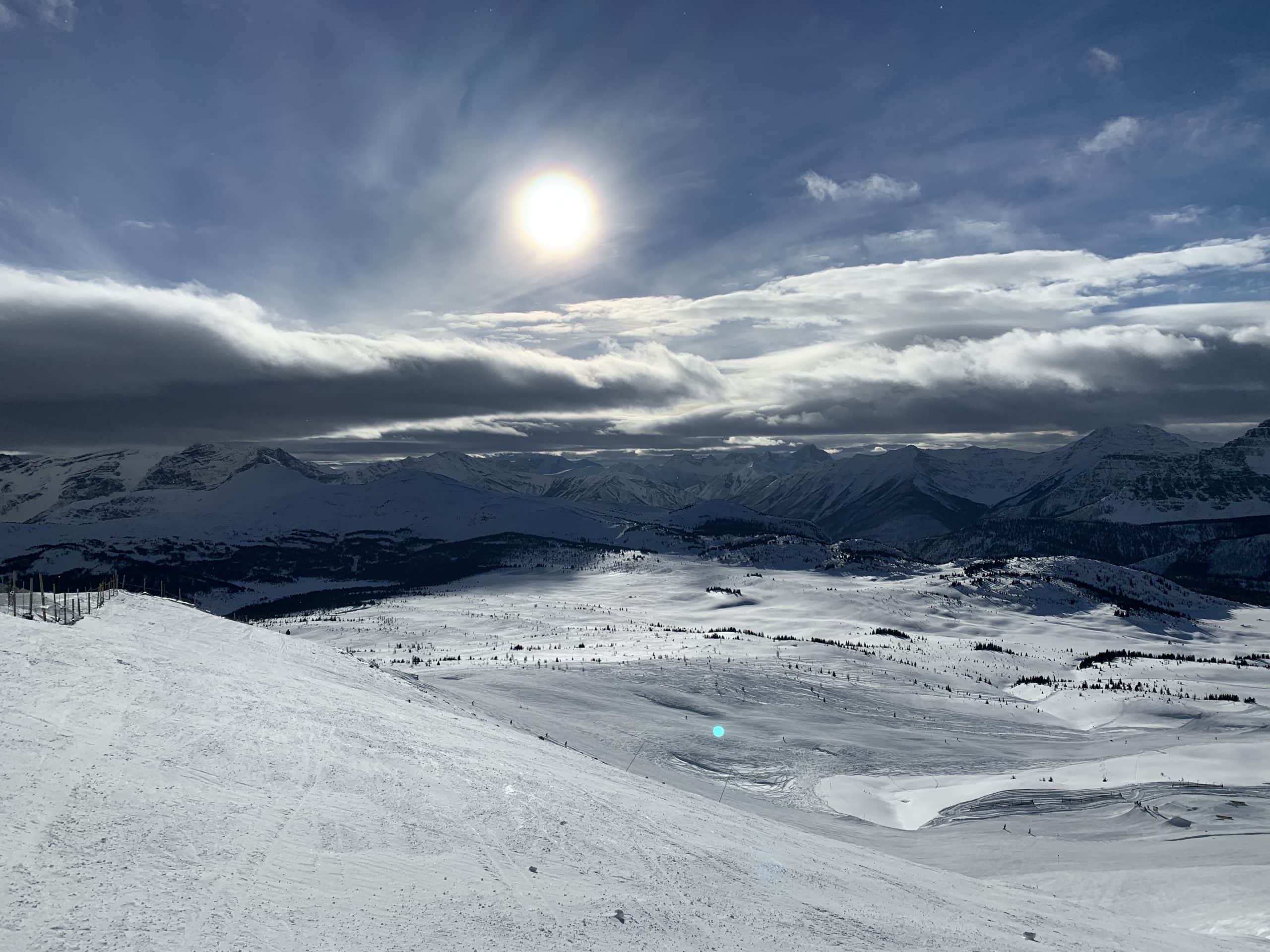 The sun shines over the snow-covered peaks and wide-open slopes of Sunshine Village, offering stunning mountain views and world-class skiing in the Canadian Rockies.