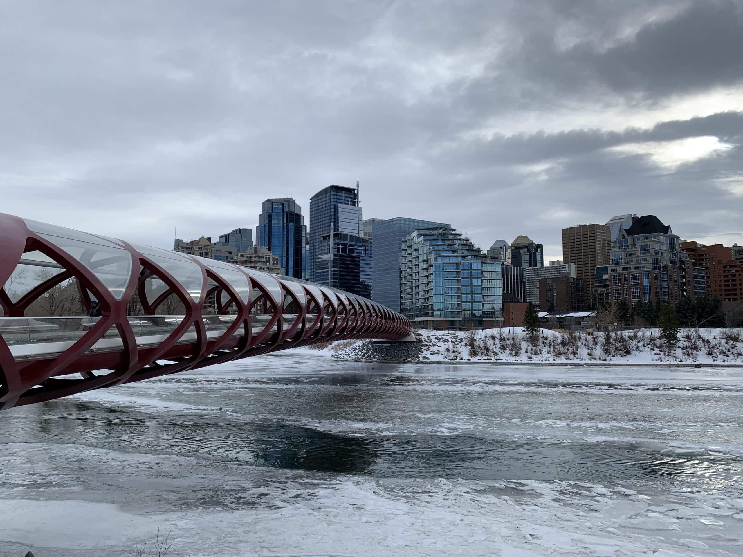 Peace Bridge spanning the icy Bow River with Calgary’s downtown skyline in the background on a cloudy winter day.