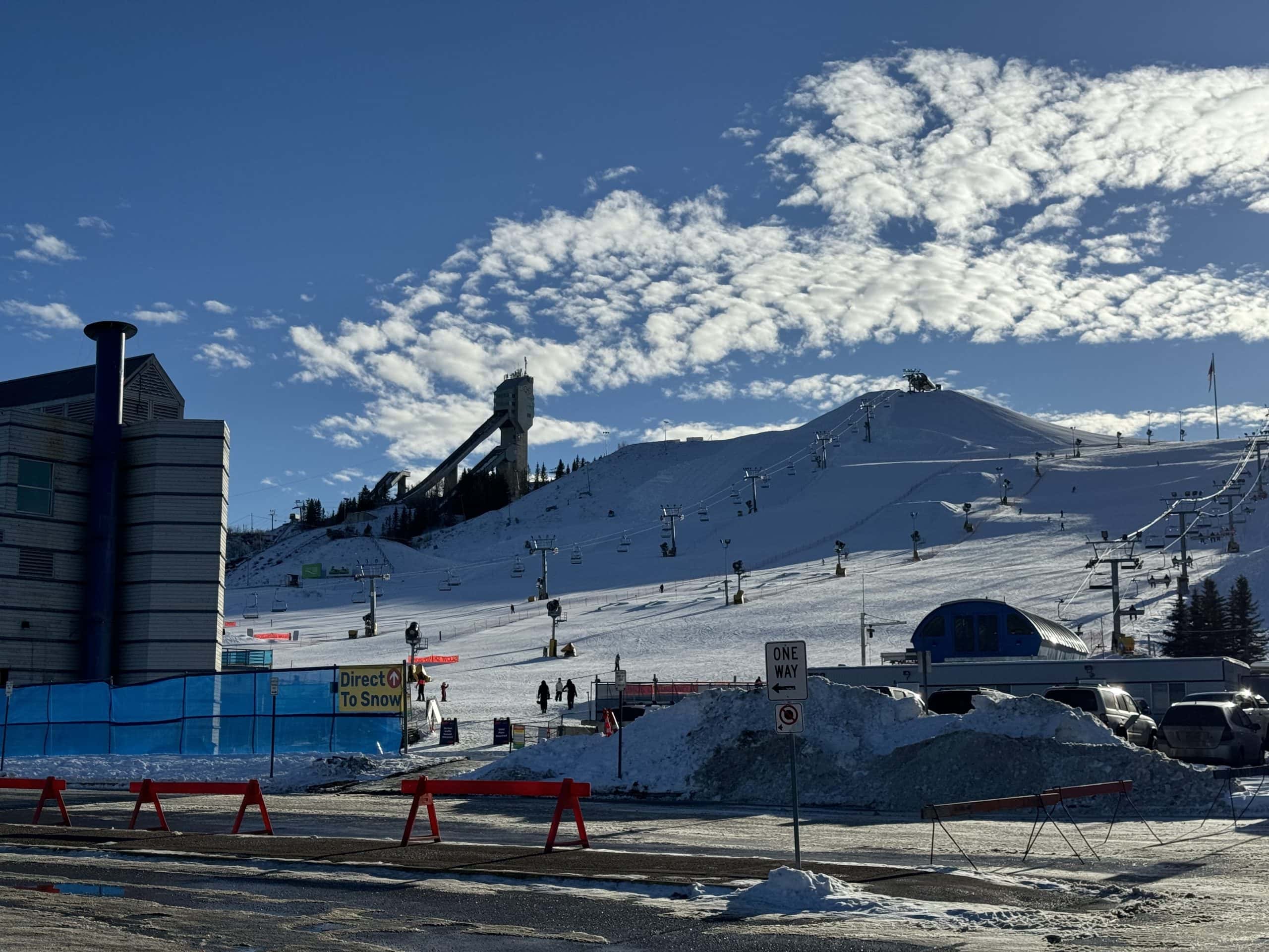Skiers and snowboarders enjoy the slopes at WinSport’s Canada Olympic Park in Calgary, with the historic ski jump tower and chairlifts set against a bright winter sky.