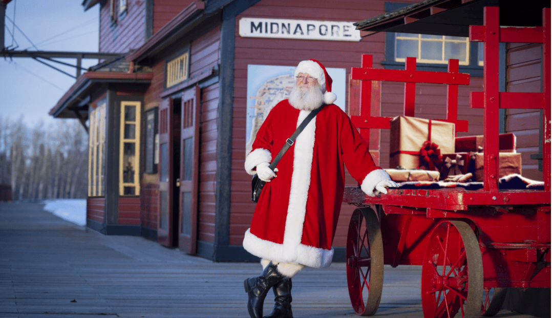 Santa poses beside a wagon of gifts at Heritage Park’s historic Midnapore station in Calgary, bringing festive charm to the Once Upon a Christmas holiday celebration.