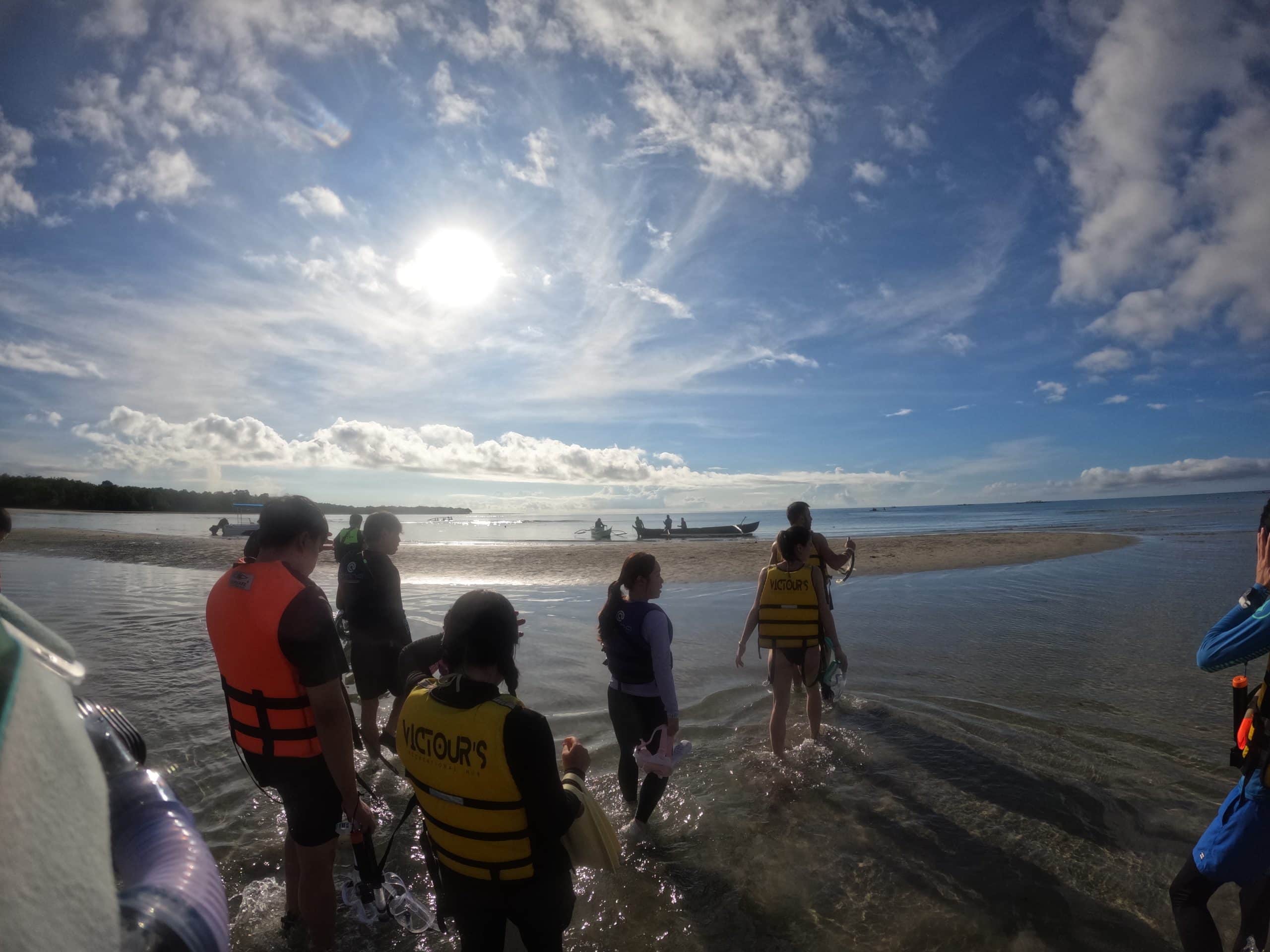 Tourists wading into the shallow water at Lila in Bohol to board small boats for the whale shark tour under a bright morning sky.