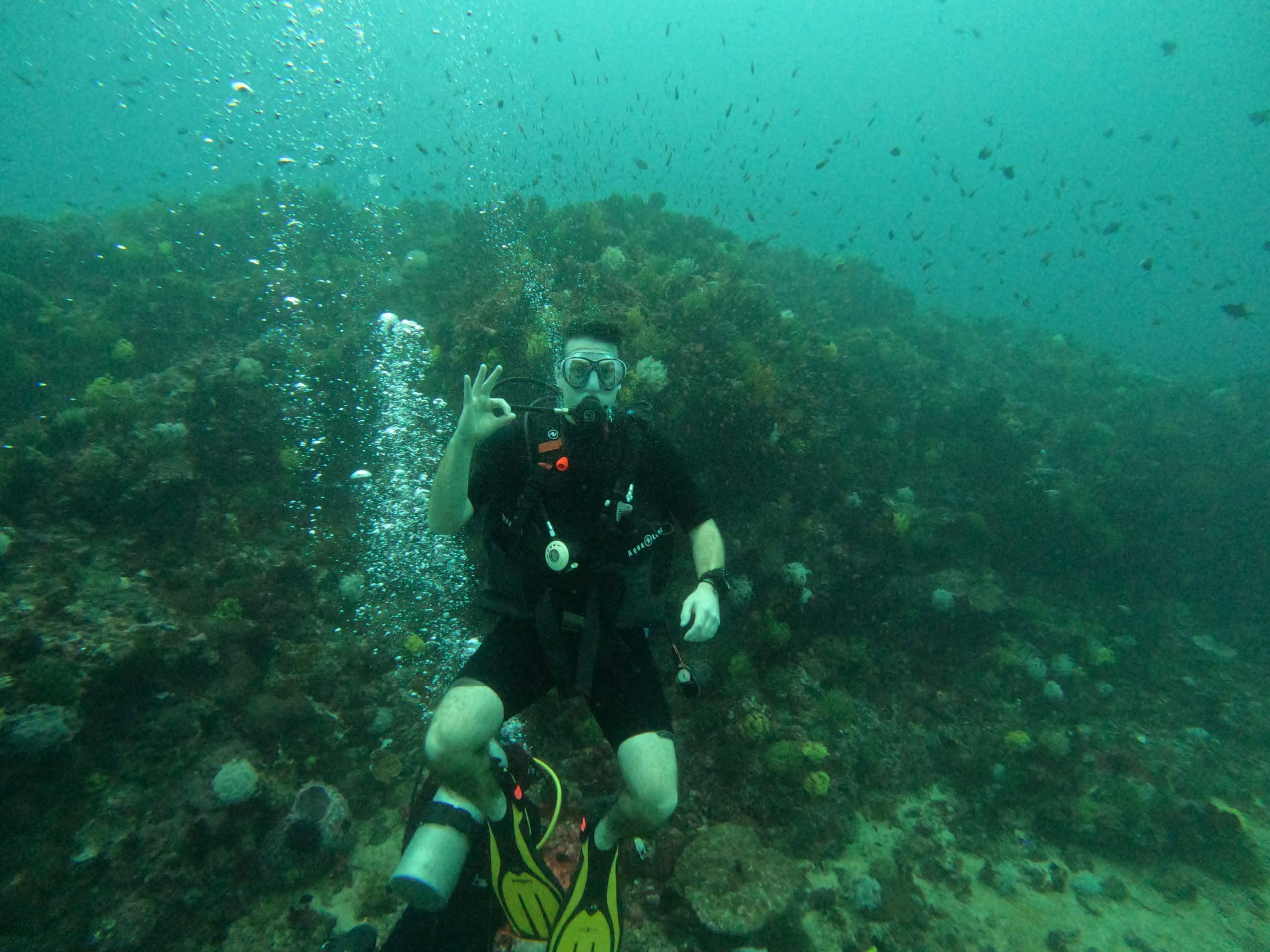 Scuba diver underwater in Sabang, Puerto Galera, Philippines, surrounded by coral reef and tropical fish during a dive.