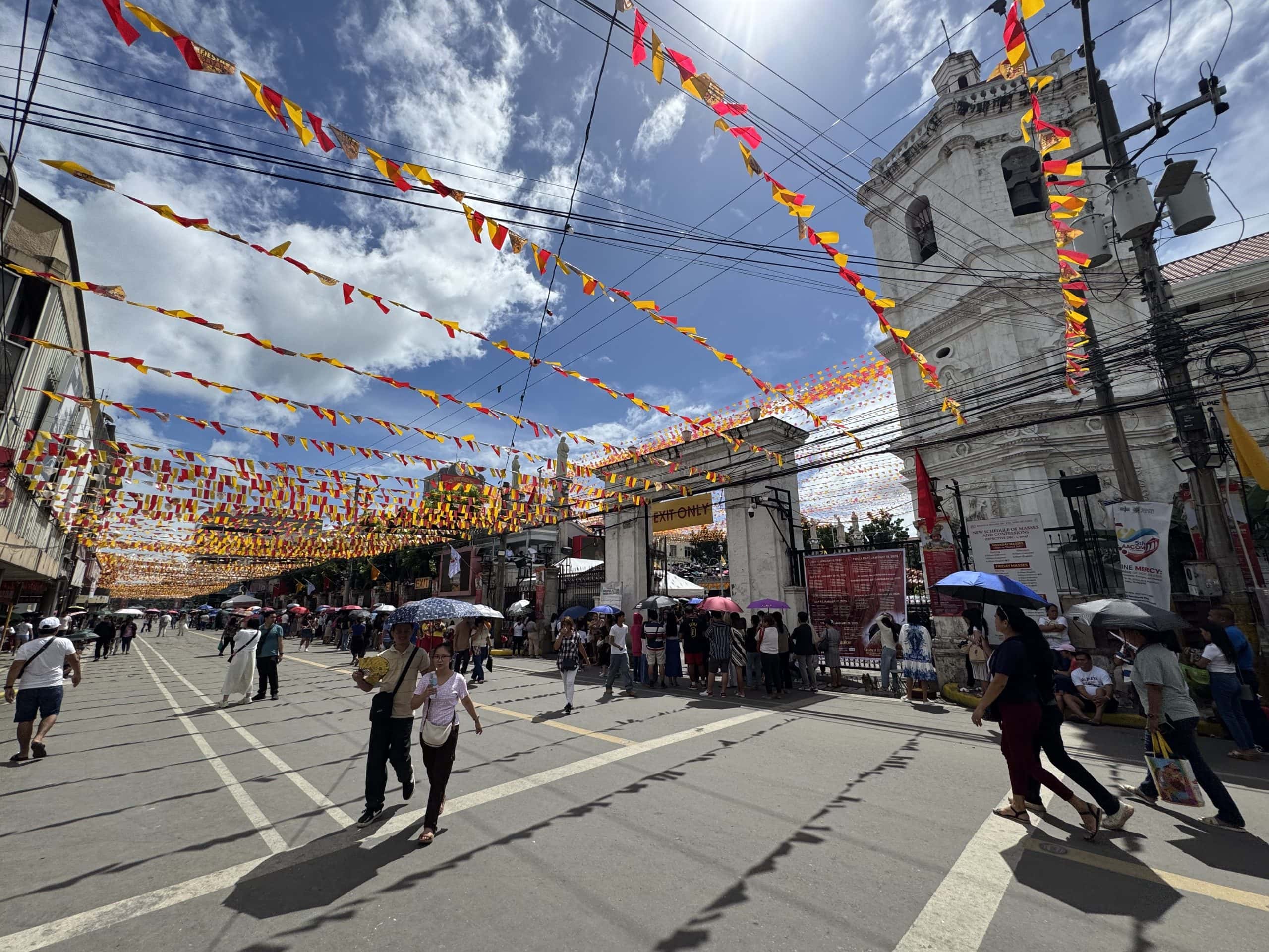 Busy street scene in Cebu City, Philippines with colourful festival banners, crowds of people, and a historic church during a lively daytime celebration.