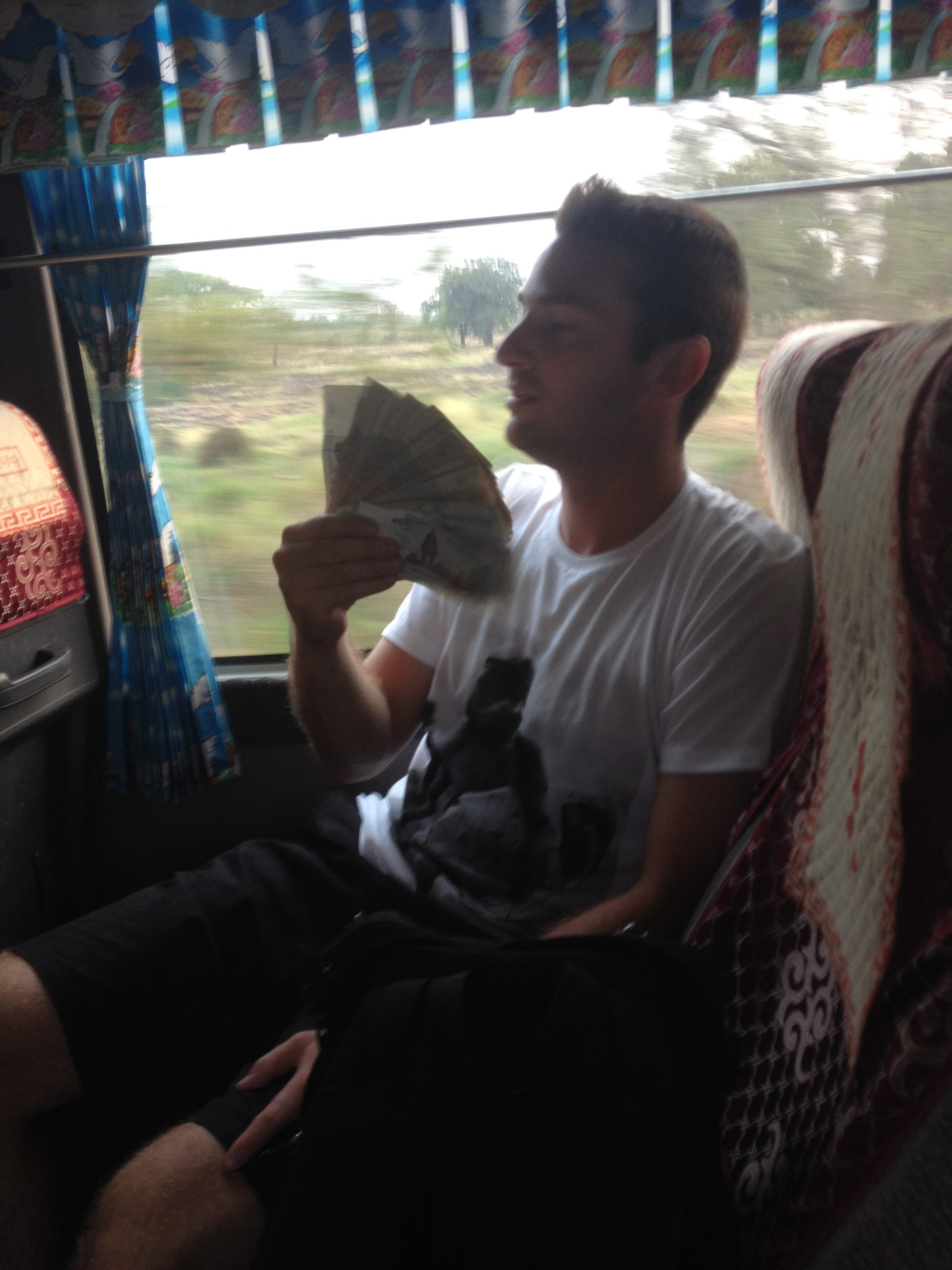 Traveler holding a stack of cash while riding a bus in Cambodia, showing how much cash is needed in some countries.