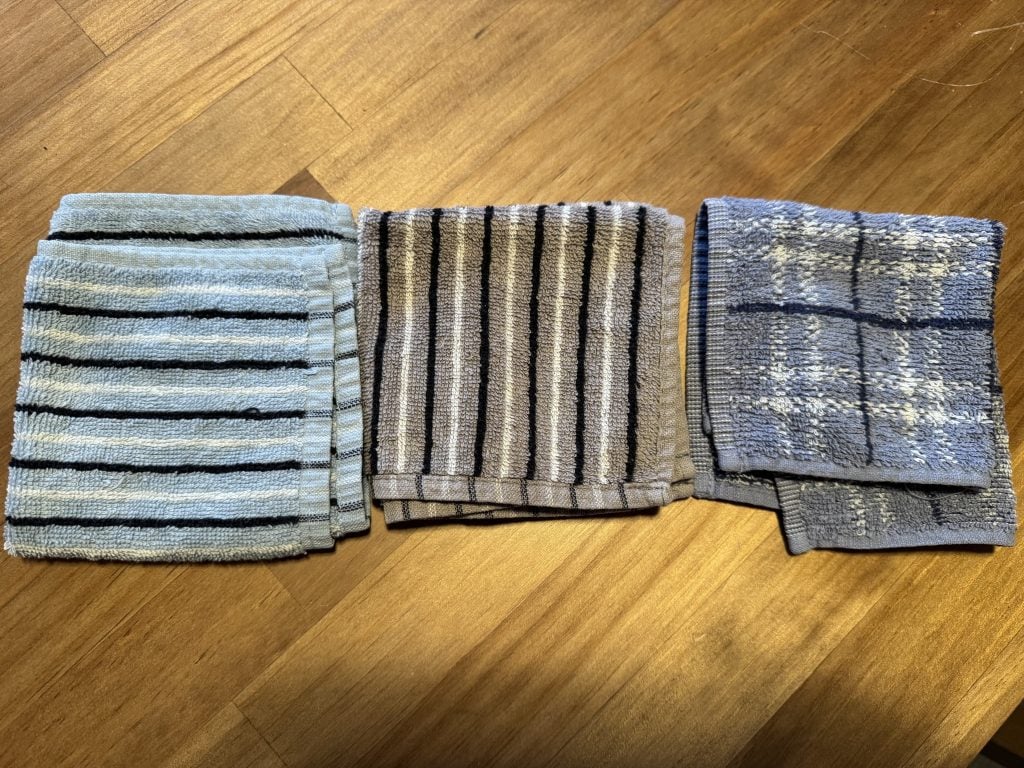 Three small cotton hand towels laid out on a wooden table, used for travel in hot and humid destinations.