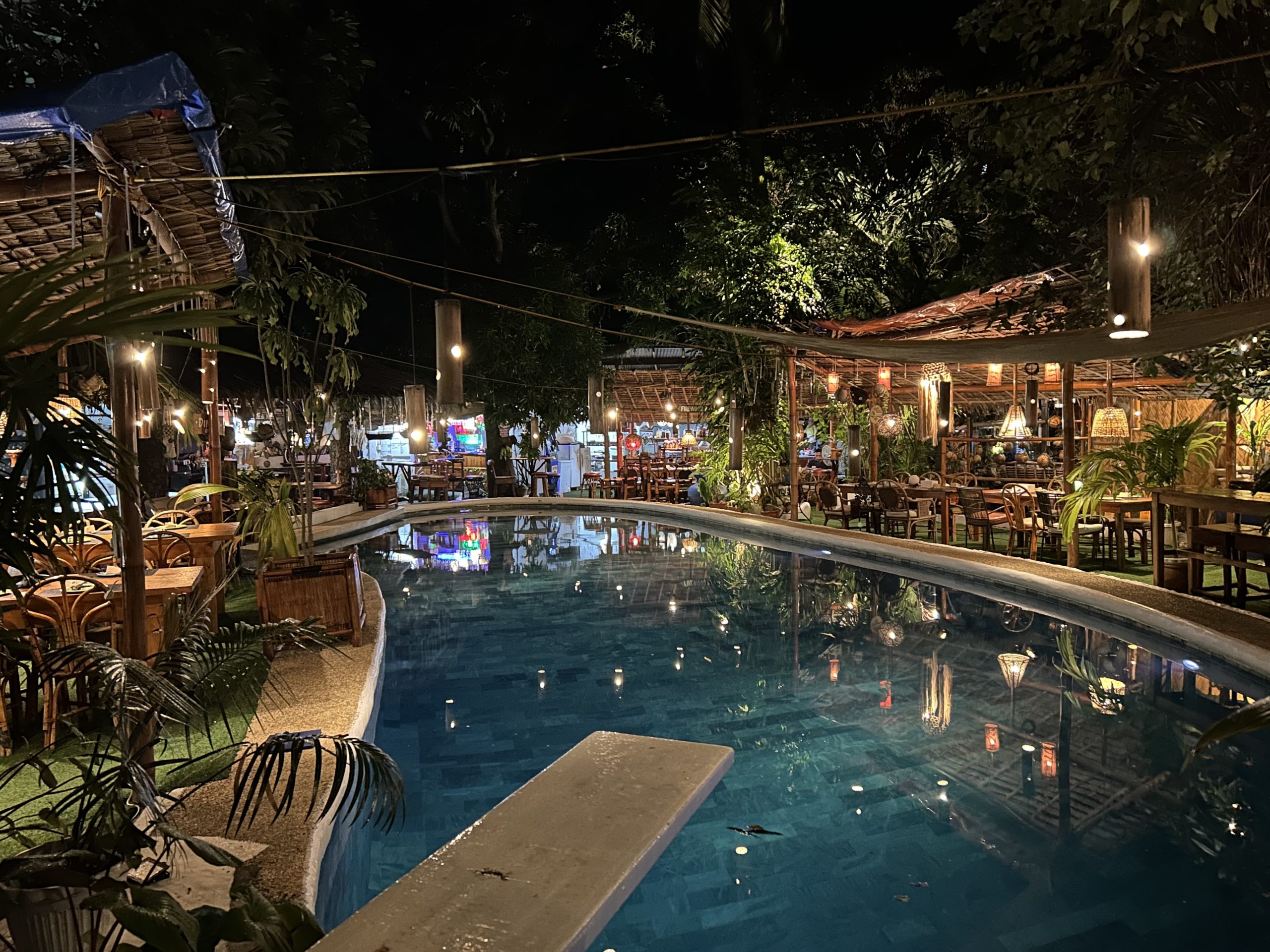 Night view of the swimming pool and open air restaurant at Big Apple Dive Resort in Sabang, Puerto Galera, showing the relaxed tropical atmosphere popular with scuba divers.
