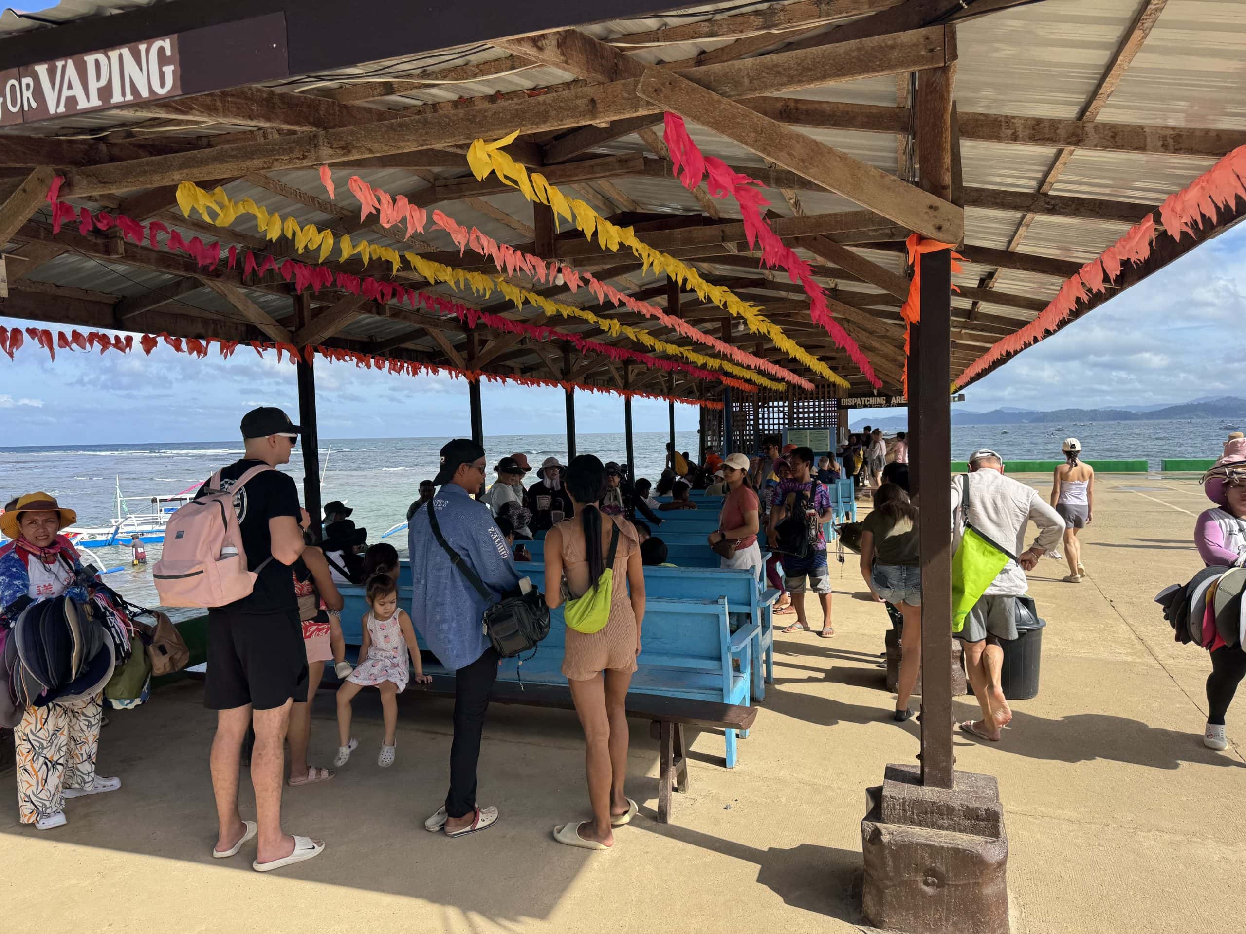 Crowds of travelers waiting at the dock near the Puerto Princesa Underground River with colorful decorations, benches, and boats along the tropical coastline in Palawan, Philippines