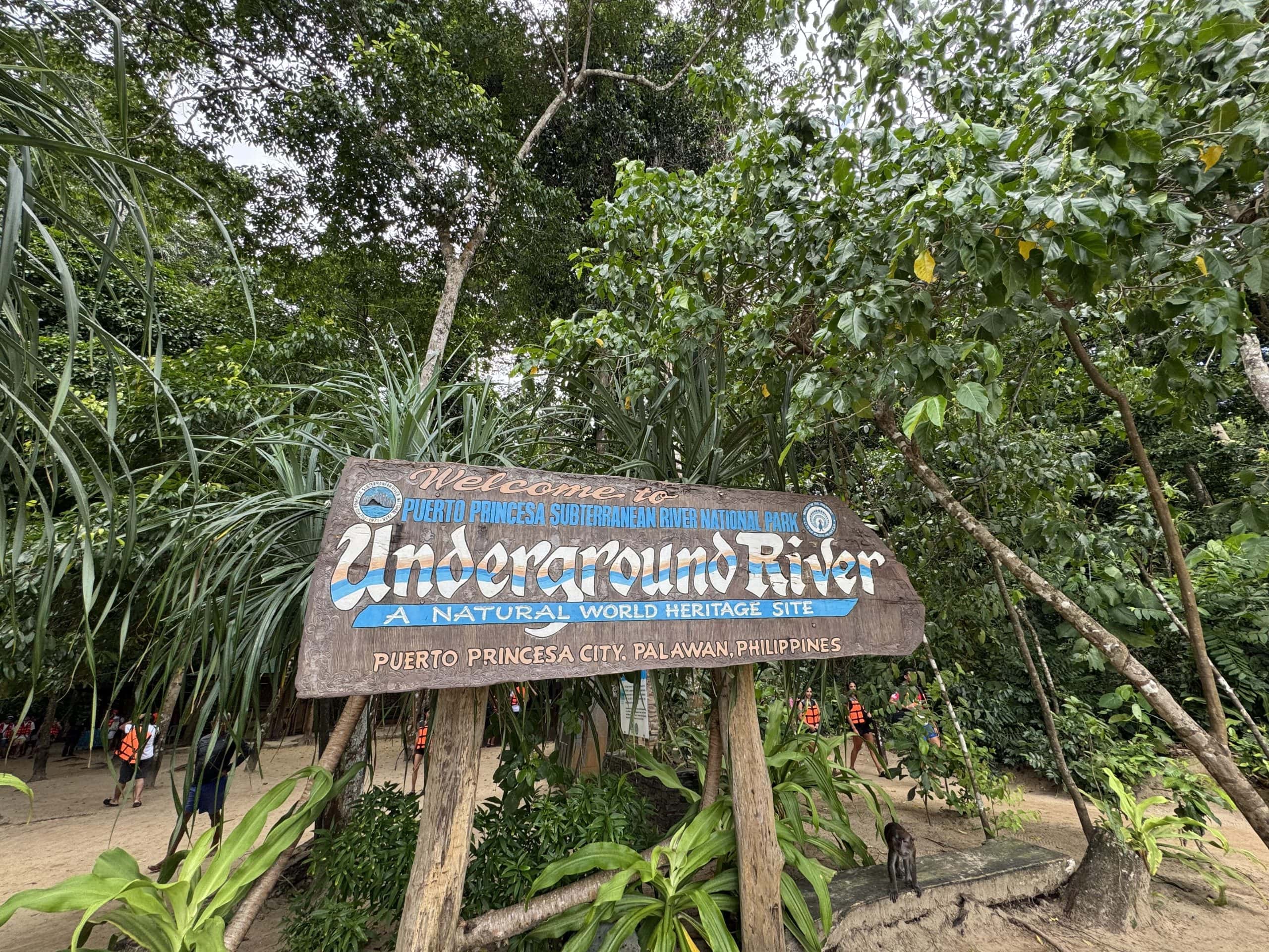 Entrance sign for the Puerto Princesa Underground River National Park surrounded by lush tropical rainforest in Palawan, Philippines with visitors preparing for the river tour