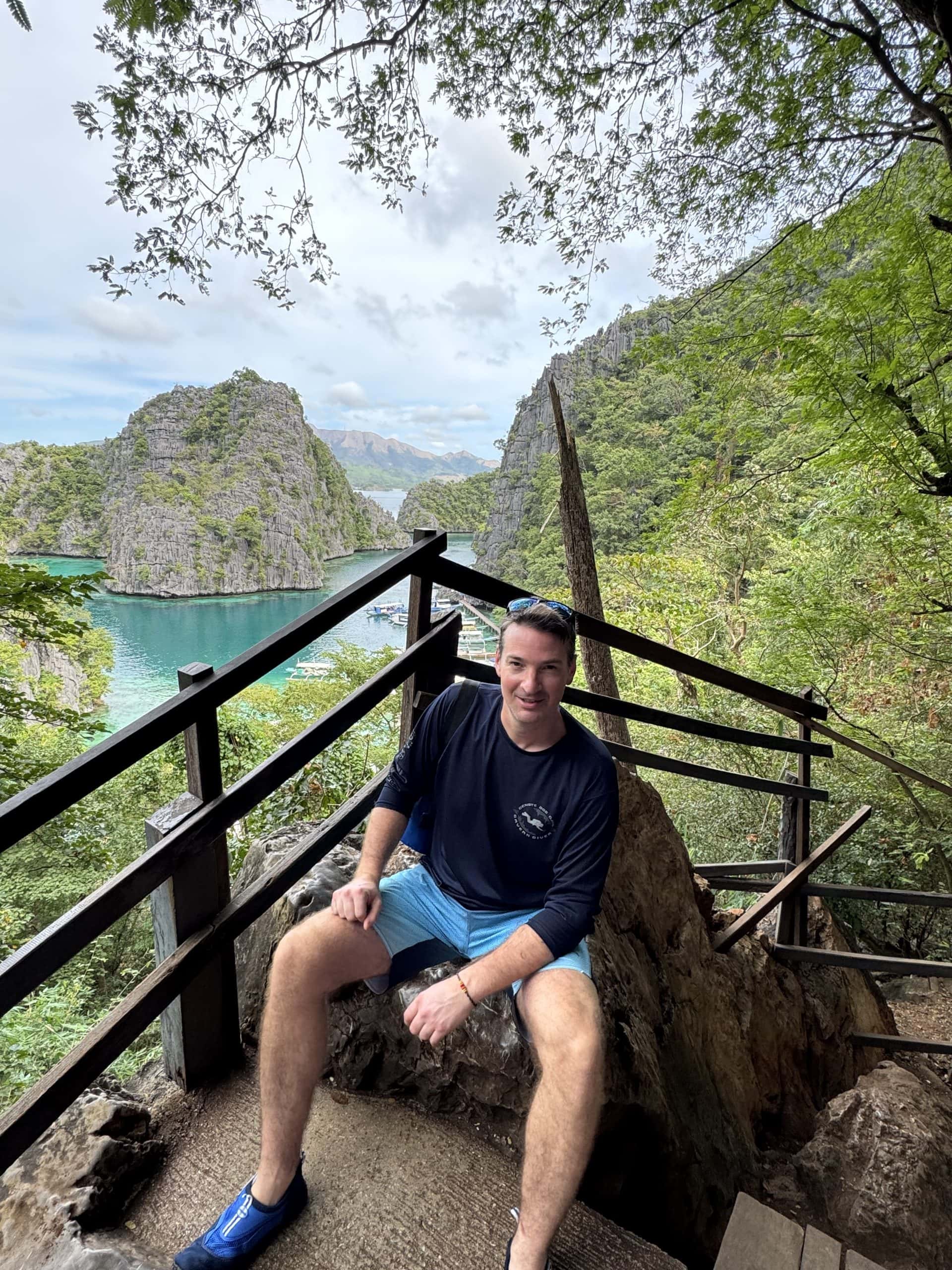 Traveler sitting at a scenic viewpoint overlooking turquoise lagoons and dramatic limestone cliffs surrounded by lush jungle in Coron, Palawan, Philippines