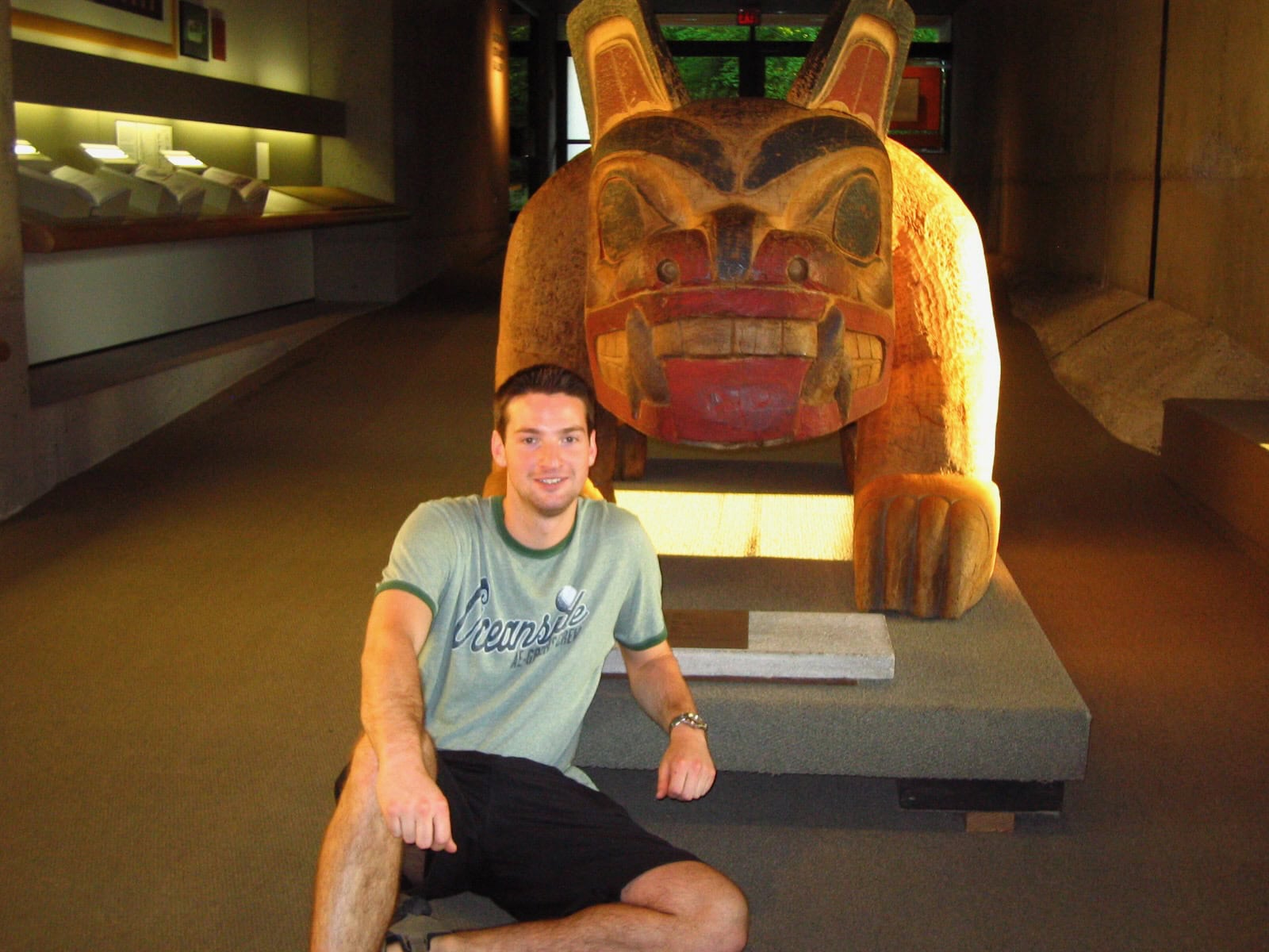 Visitor posing beside a traditional Northwest Coast Indigenous carved animal sculpture inside the Museum of Anthropology at the University of British Columbia in Vancouver