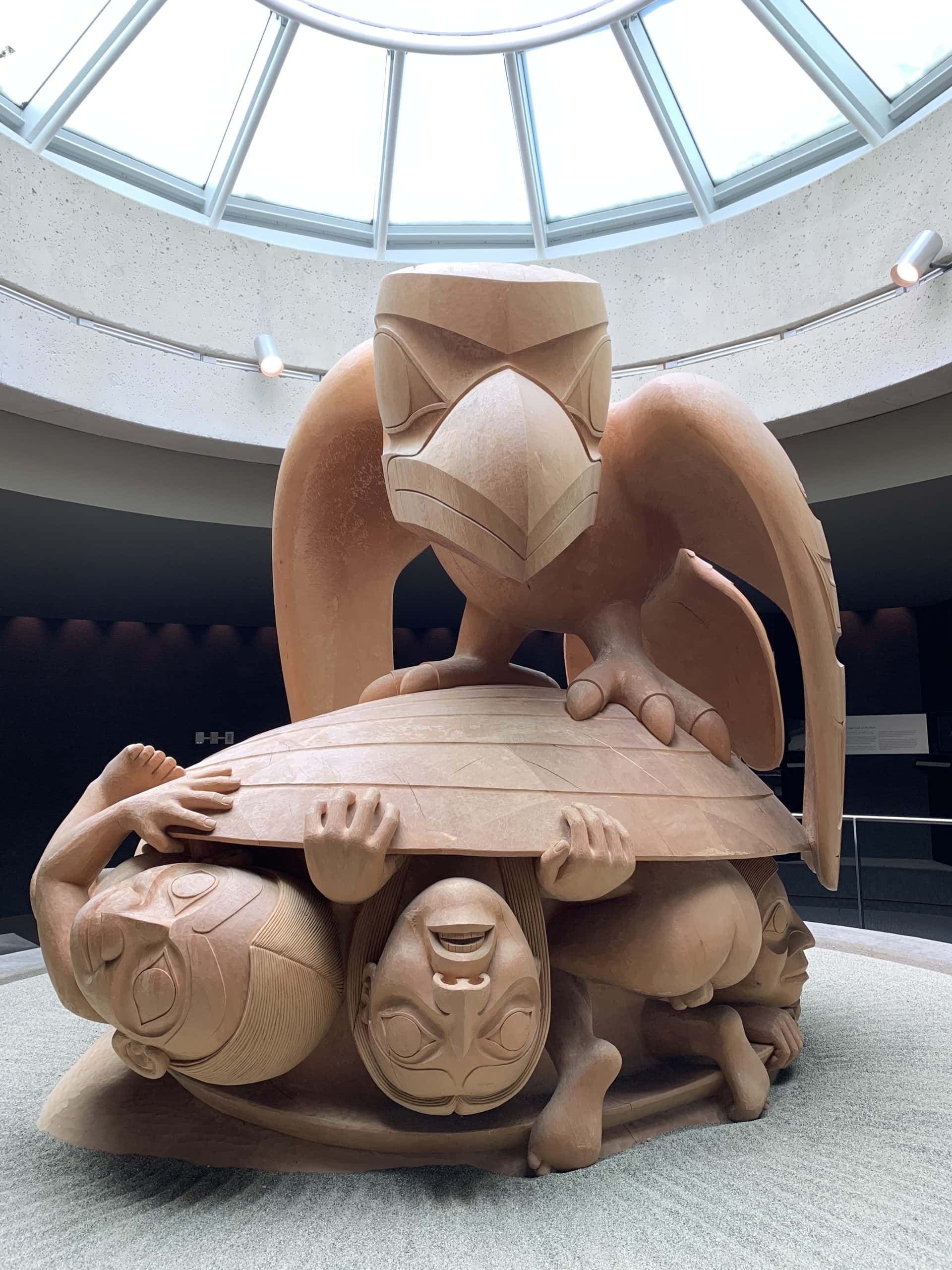 Large Northwest Coast Indigenous sculpture inside the Museum of Anthropology at the University of British Columbia featuring a carved eagle and human figures beneath a glass dome skylight