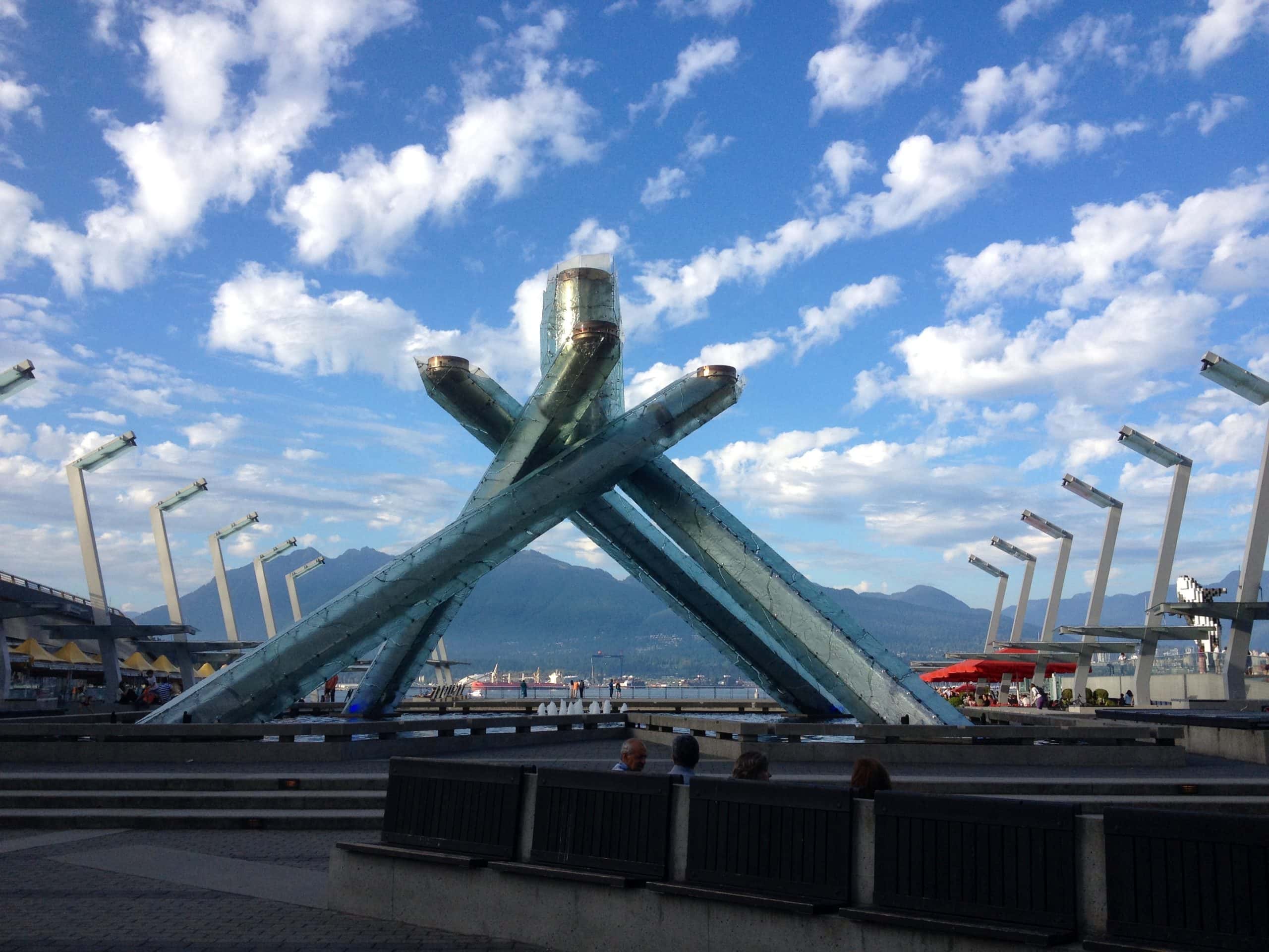 Olympic Cauldron at Jack Poole Plaza in Vancouver with the North Shore Mountains and waterfront views under a blue sky with scattered clouds