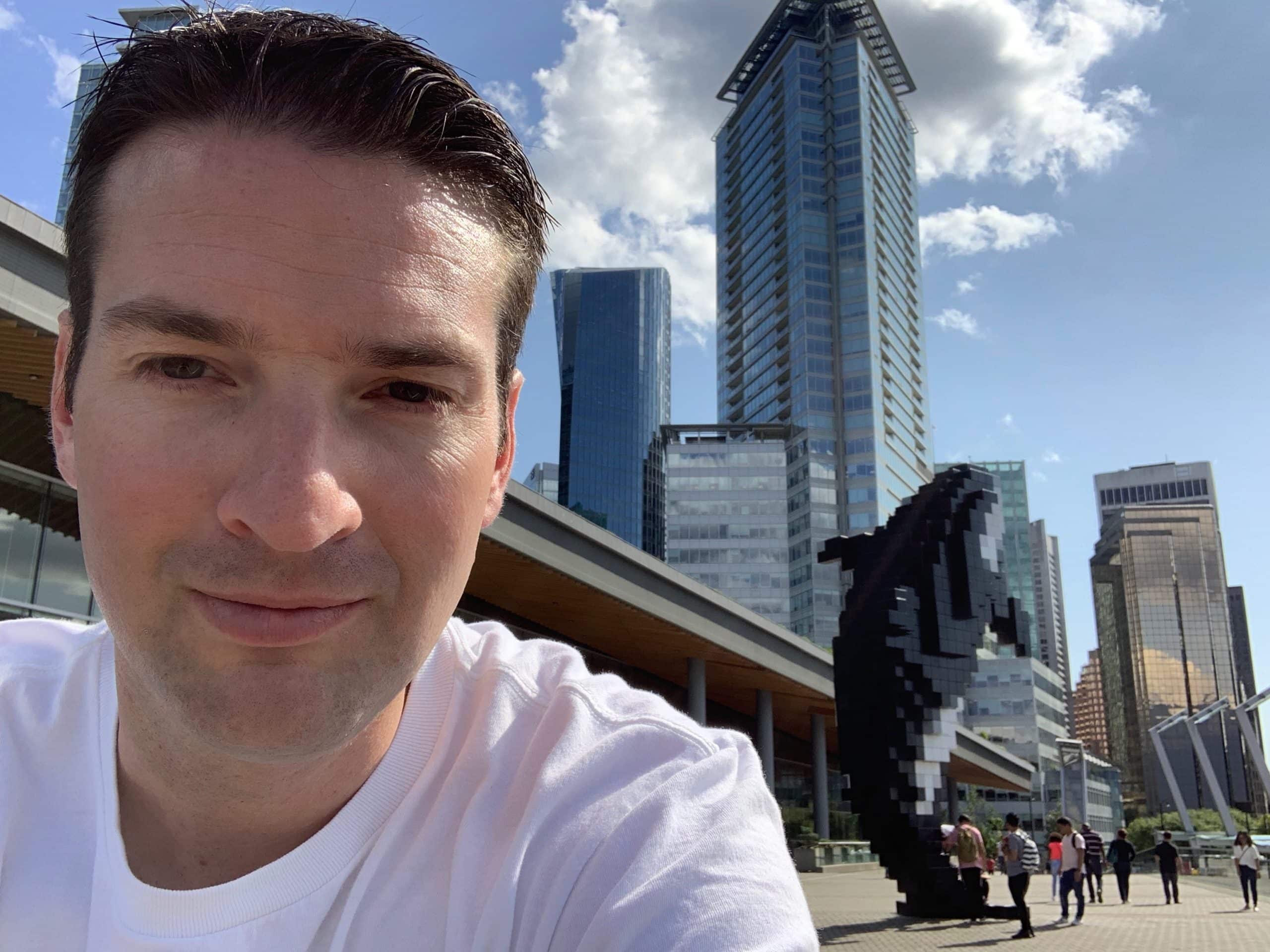 Selfie at the Digital Orca sculpture in downtown Vancouver with modern skyscrapers and waterfront promenade at Jack Poole Plaza near Canada Place
