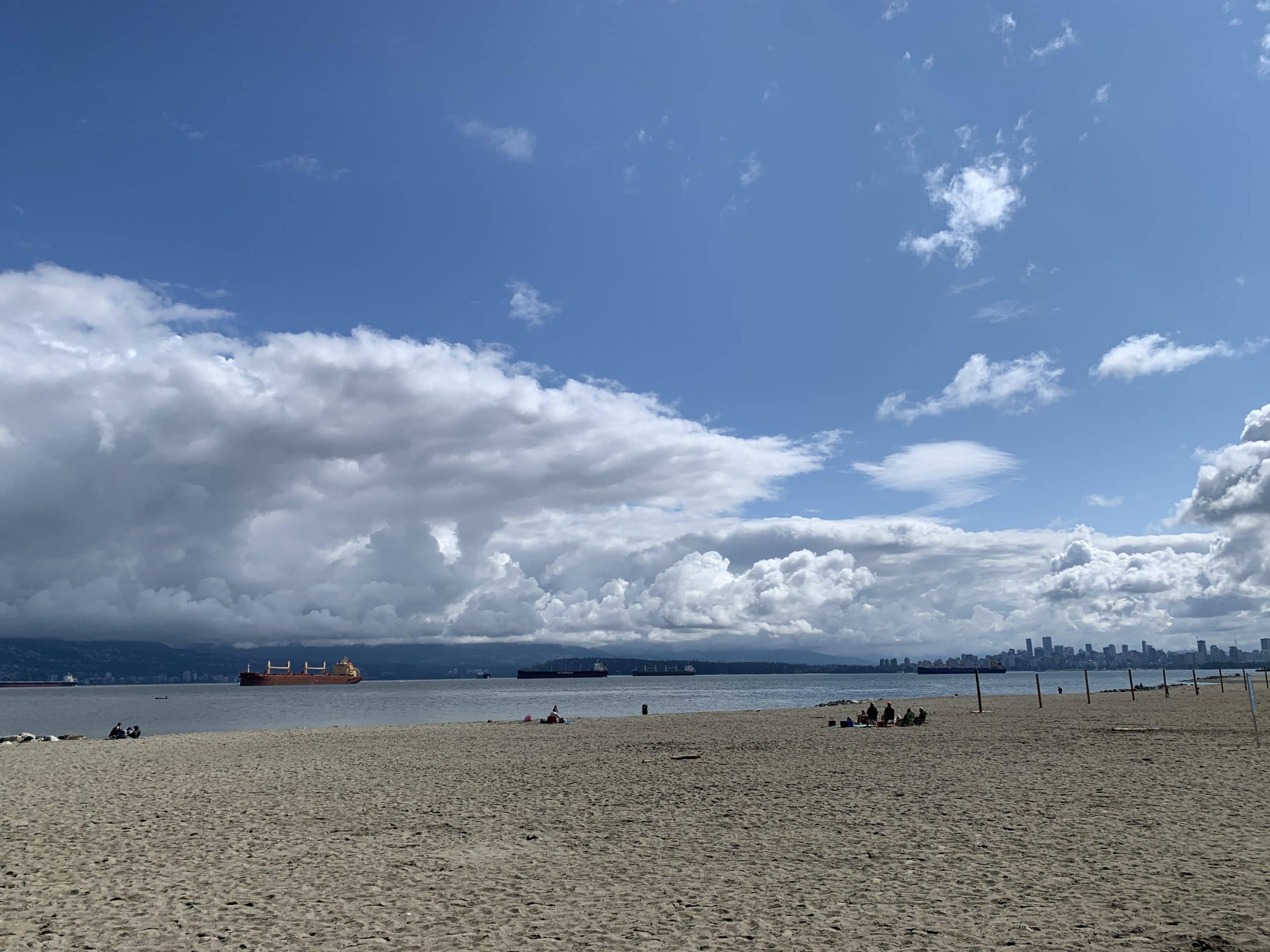 Wide sandy beach at Spanish Banks in Vancouver with cargo ships in English Bay and views of the distant downtown skyline under dramatic coastal clouds