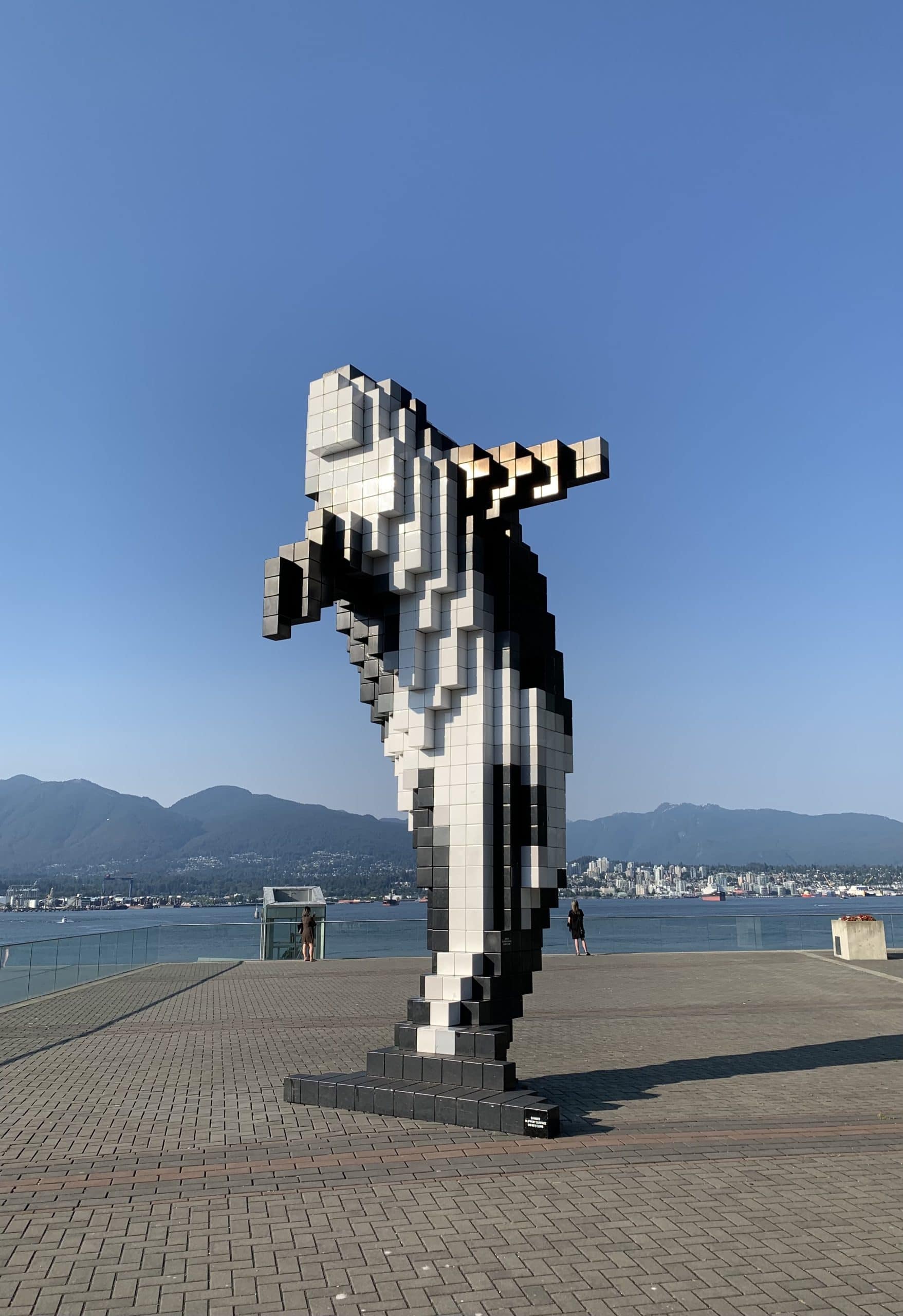 Digital Orca sculpture at Jack Poole Plaza in Vancouver with Burrard Inlet, North Shore Mountains, and the city skyline in the background