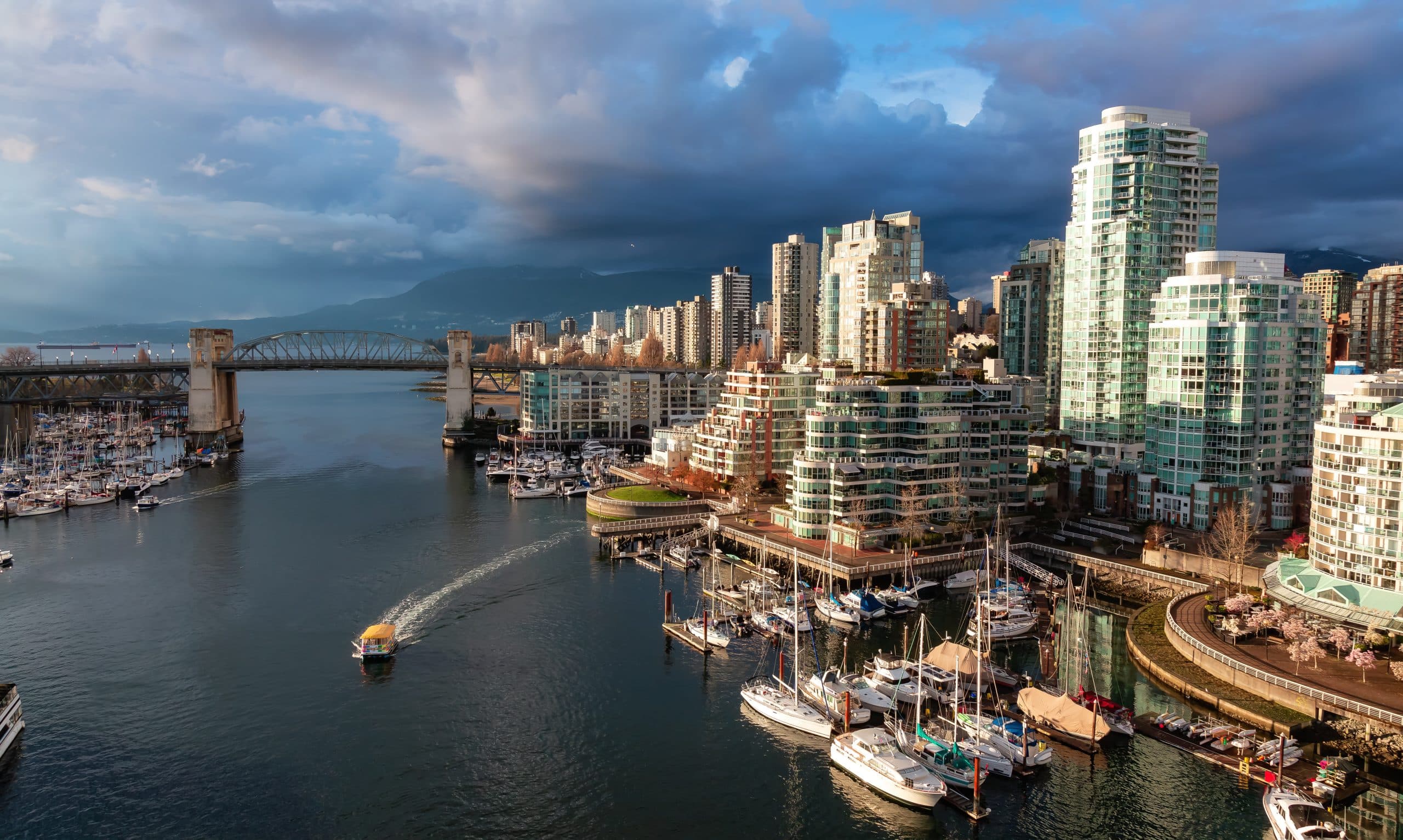 Aerial view of False Creek in Vancouver with Granville Bridge, waterfront marinas, sailboats, and modern residential towers along the shoreline
