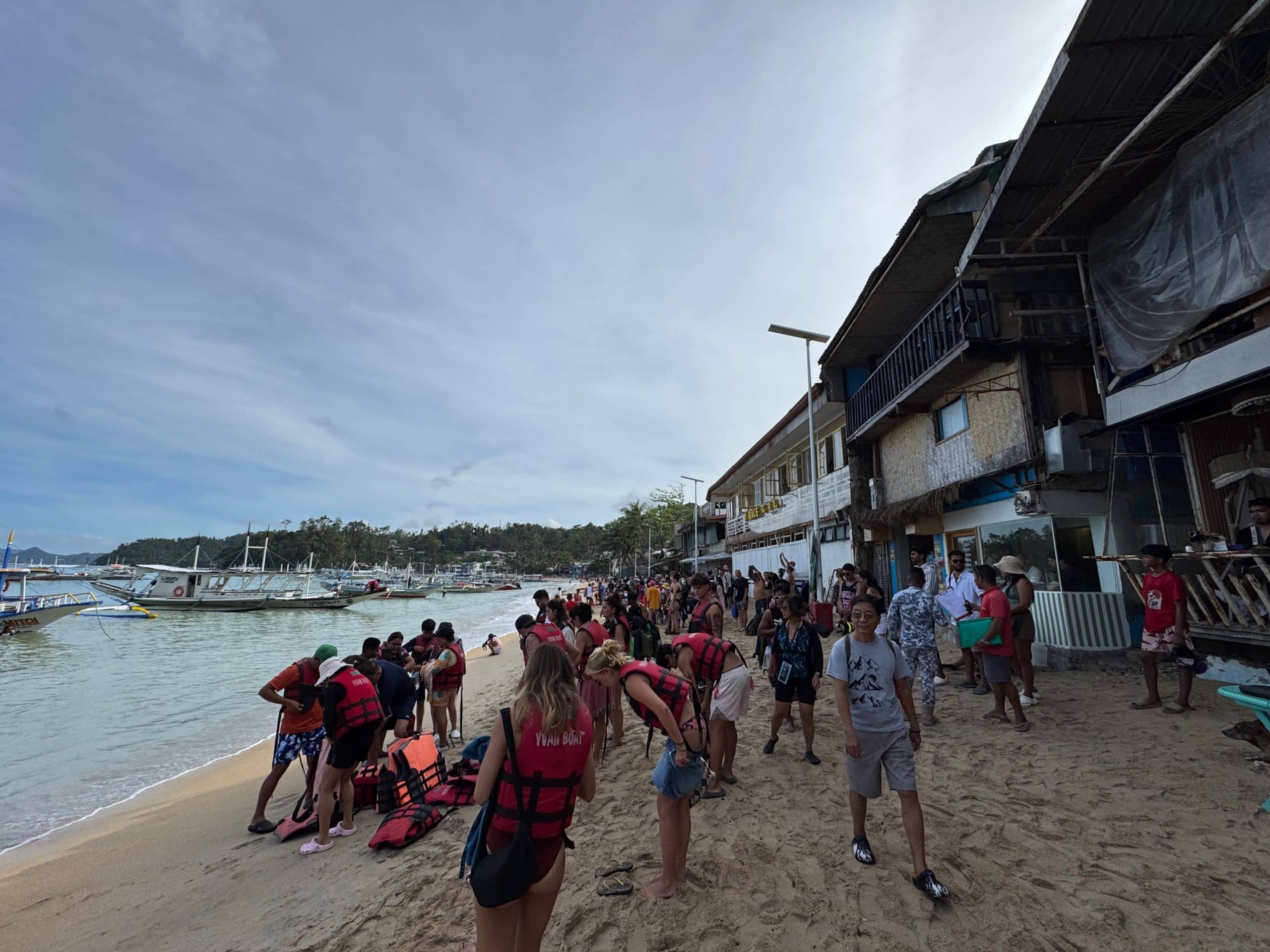 Busy El Nido beach scene with tourists preparing for island hopping tours as traditional boats line the shore in Palawan Philippines