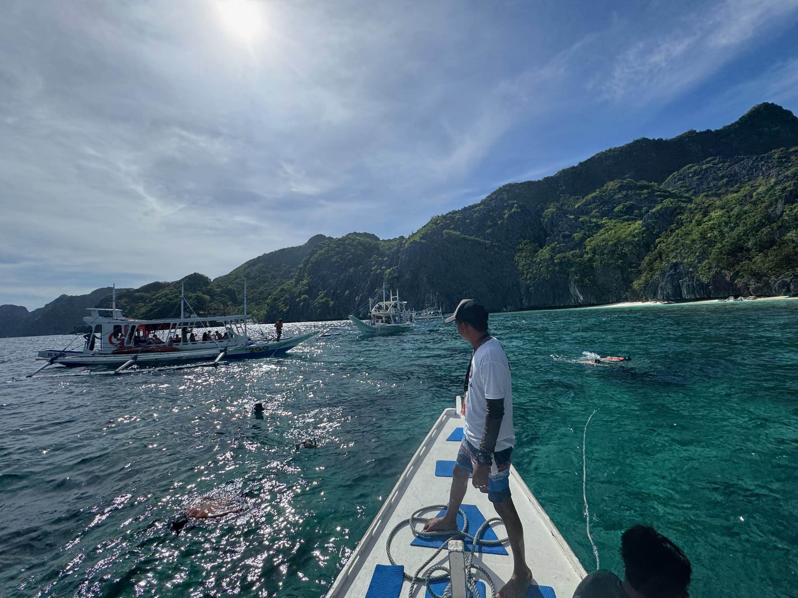 Snorkeling in El Nido with crystal clear turquoise water and traditional boats anchored near lush limestone islands in Palawan Philippines