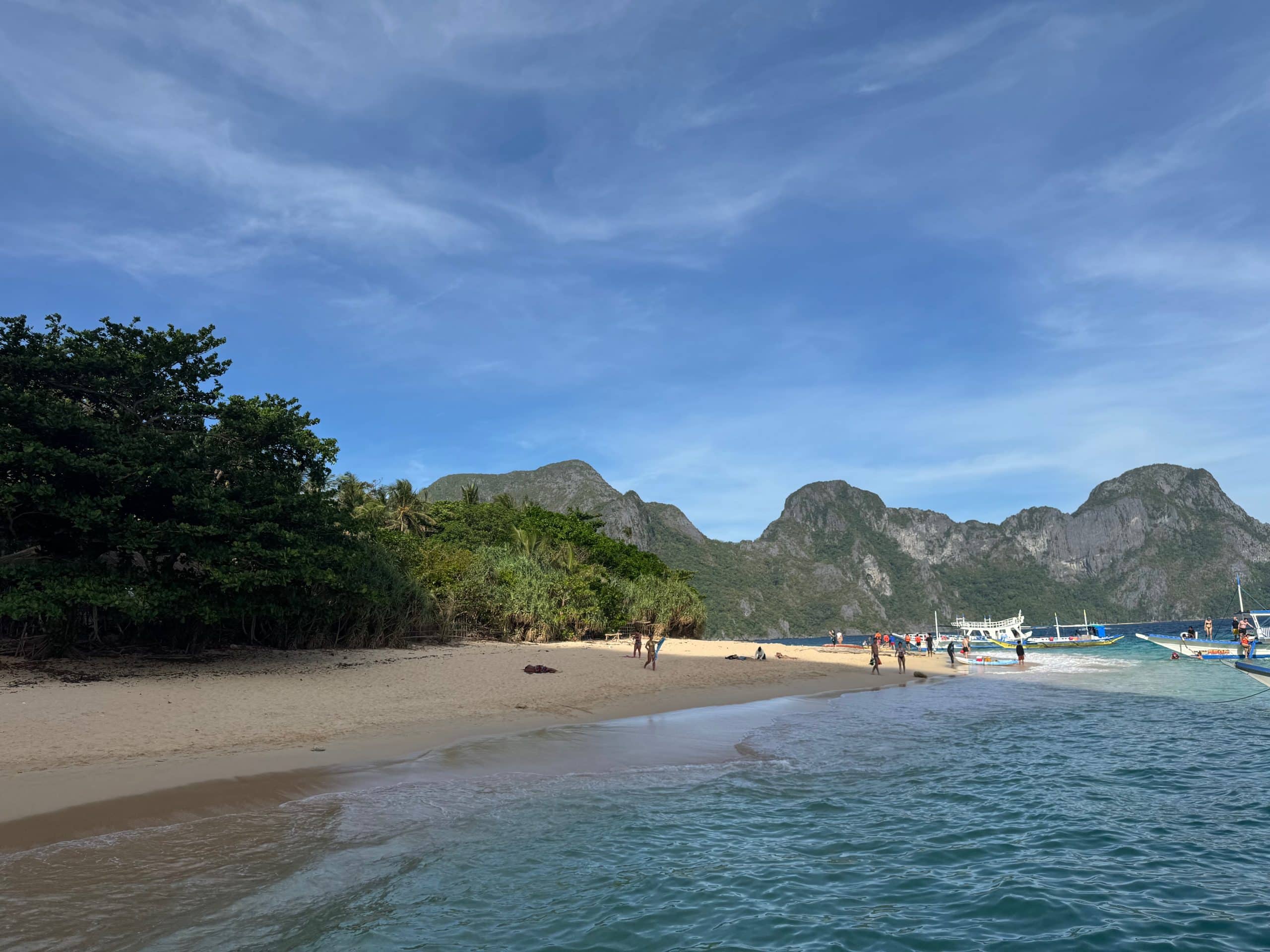 Helicopter Island in El Nido with a wide white sand beach clear turquoise water and limestone mountains in the background in Palawan Philippines