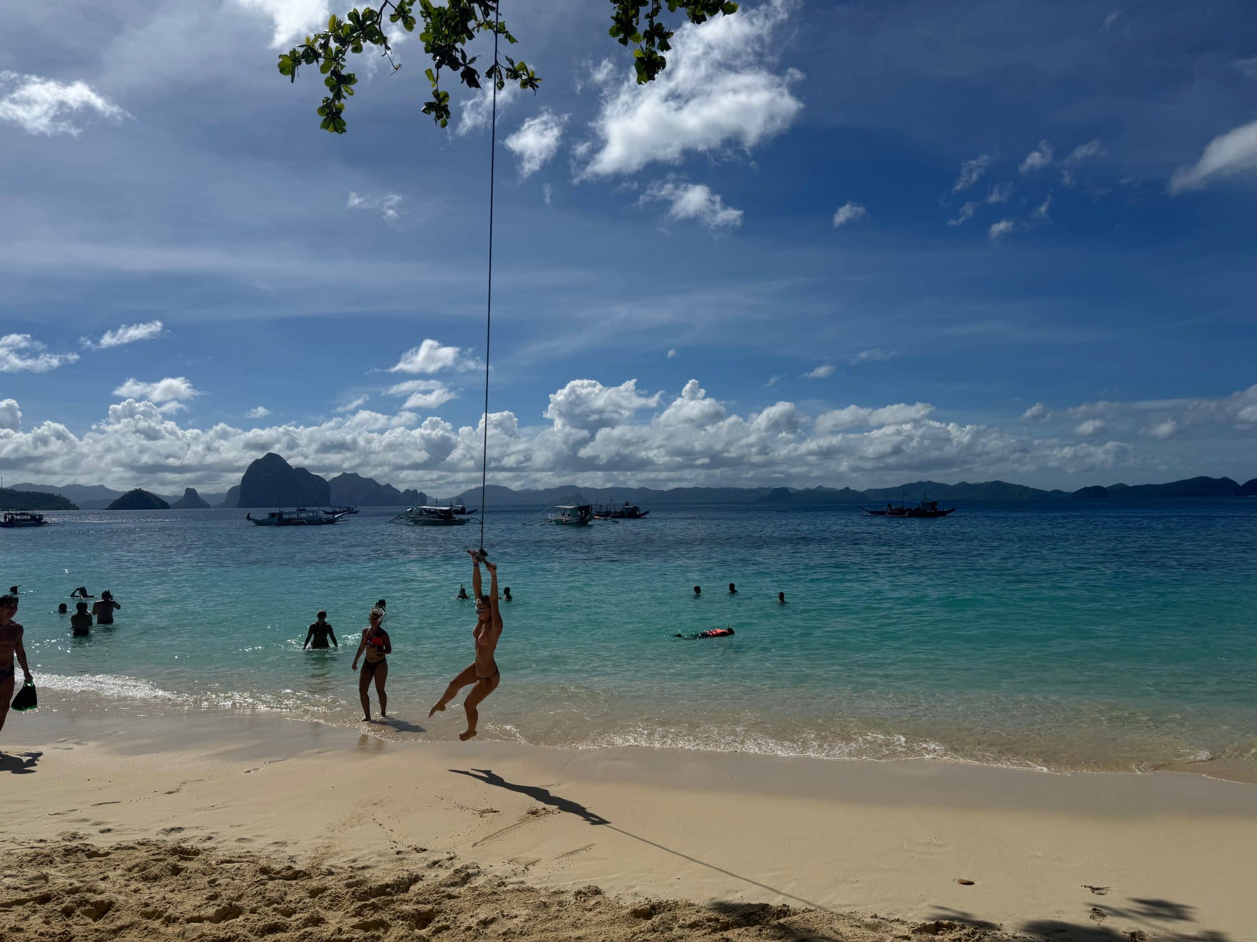 Relaxing on a beautiful El Nido beach with clear water, boats in the distance, and a rope swing by the shore